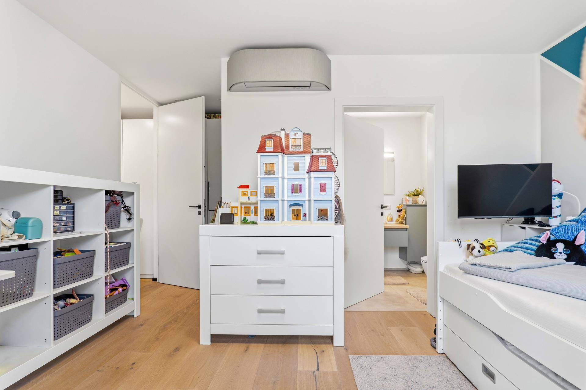 Helles Kinderzimmer mit Spielzeug, Stauraum und Blick auf das angrenzende Badezimmer.