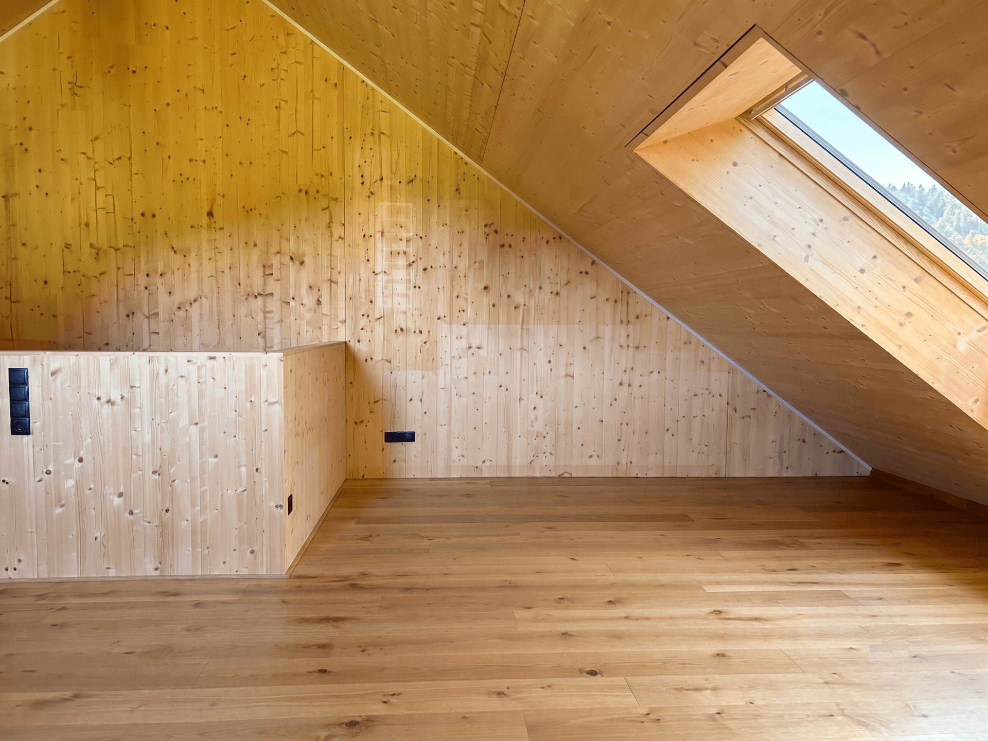Geräumiger Dachboden mit Holzwänden, Holzboden und großem Dachfenster.