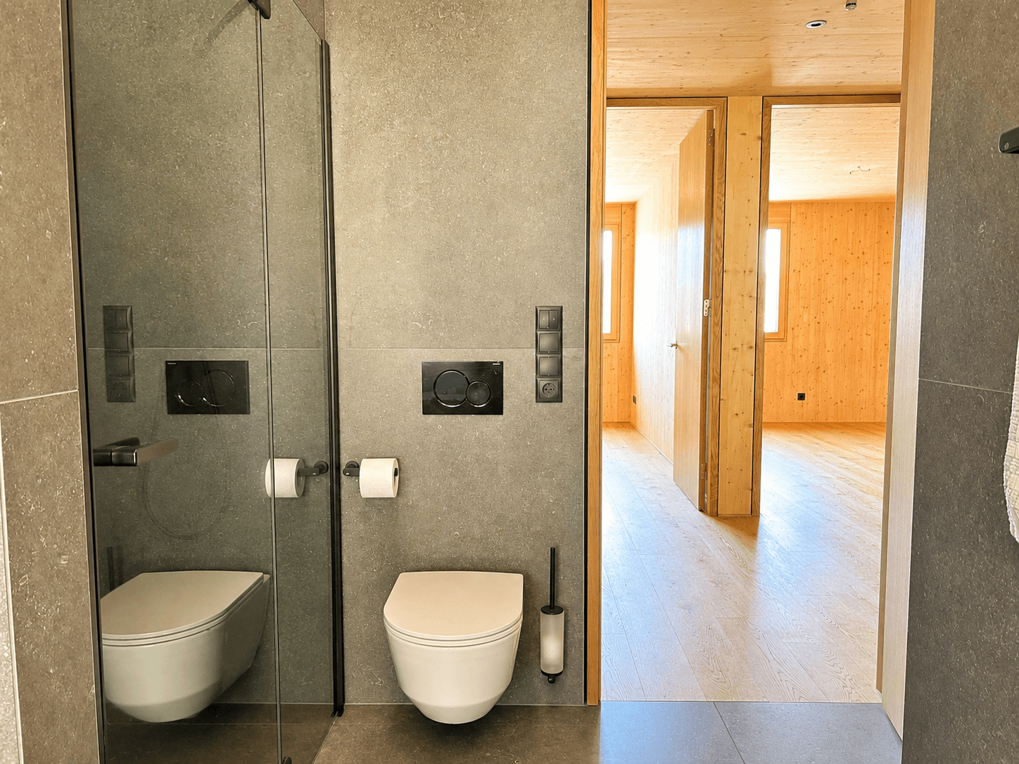 Modernes Badezimmer mit grauen Fliesen, wandhängendem WC und ebenerdiger Dusche.