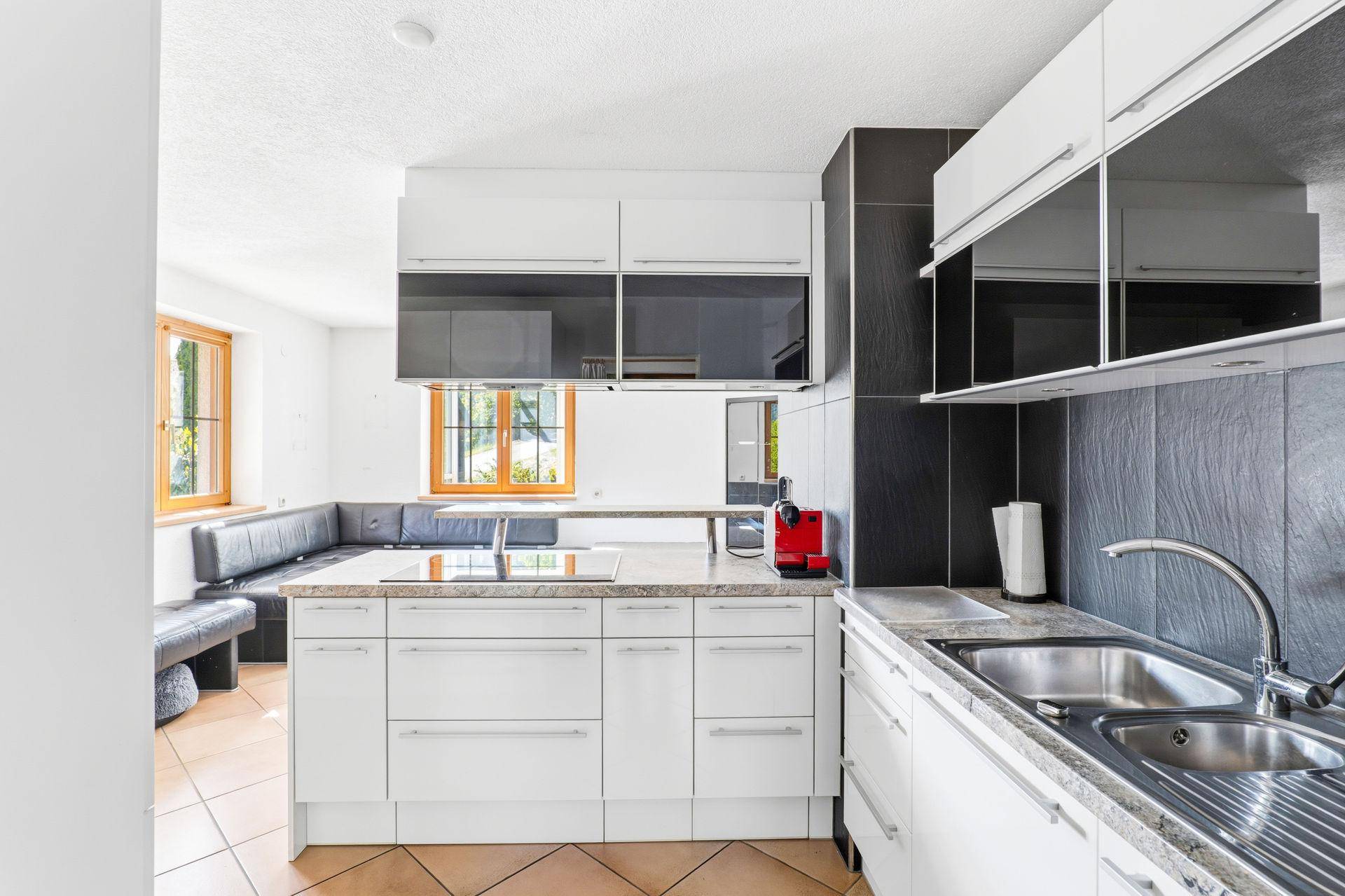 Moderne Küche mit weißen Hochglanzfronten, dunkler Arbeitsplatte und integriertem Essbereich.