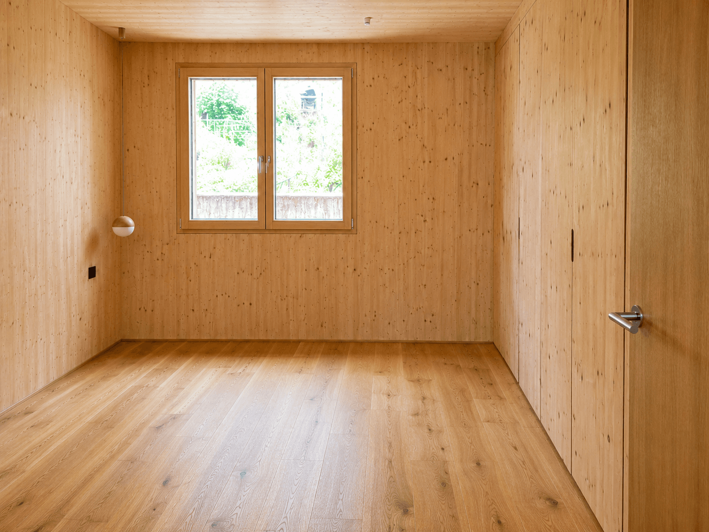 Helles Schlafzimmer mit Holzwänden, Holzboden und großem Fenster zum Garten.