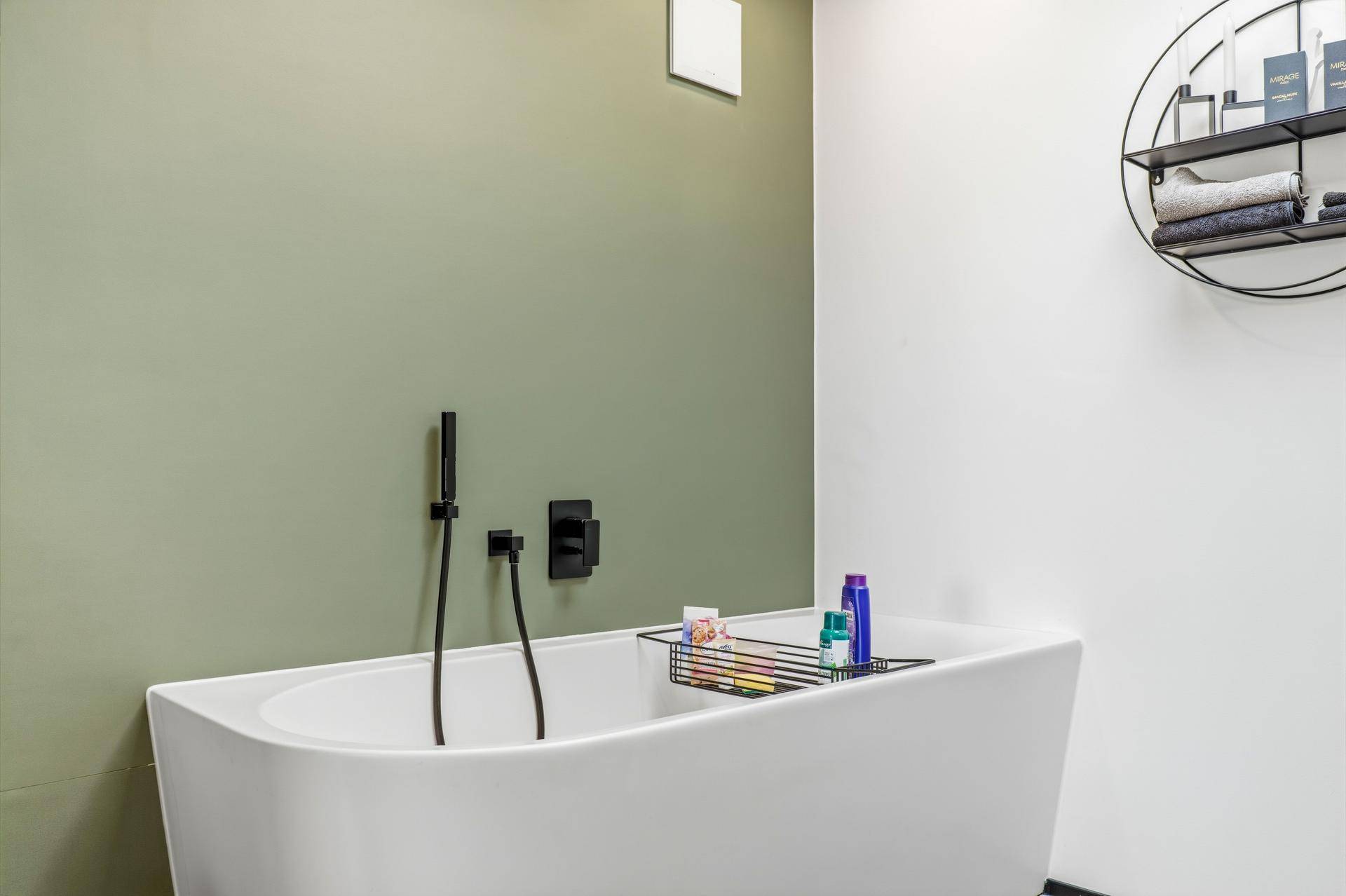Freistehende Badewanne vor einer mintgrünen Wand mit schwarzer Armatur.