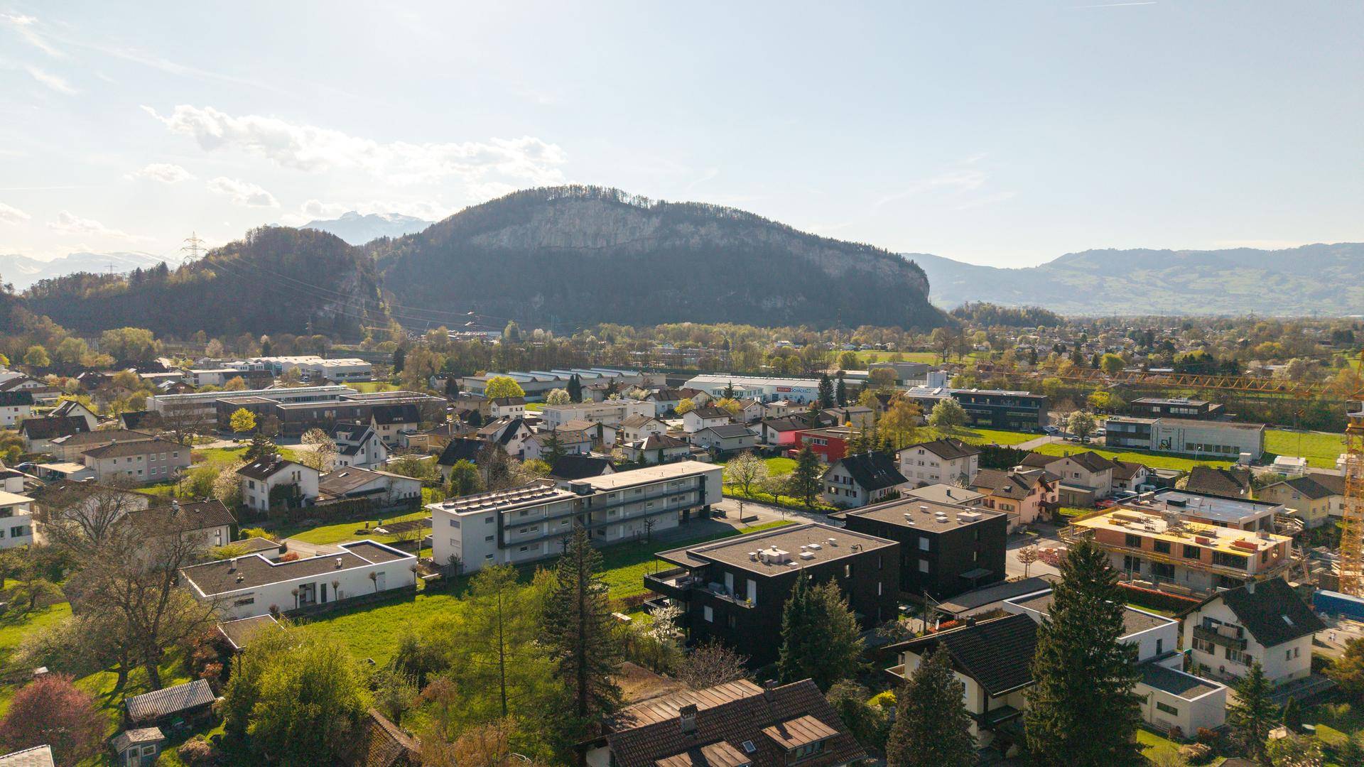 Panoramablick auf eine Wohngegend mit Bergen und viel Grün unter blauem Himmel.