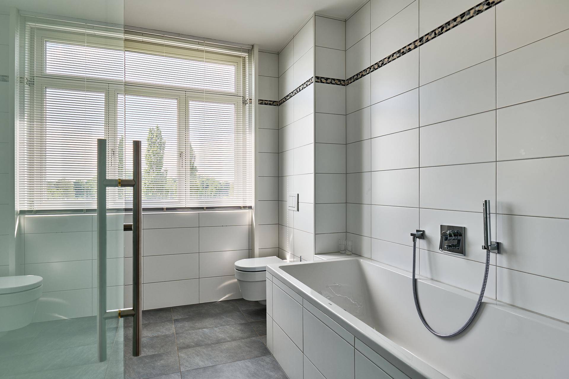 Modernes Badezimmer mit weißen Wandfliesen, einer Badewanne und einem Fenster für natürliches Licht.
