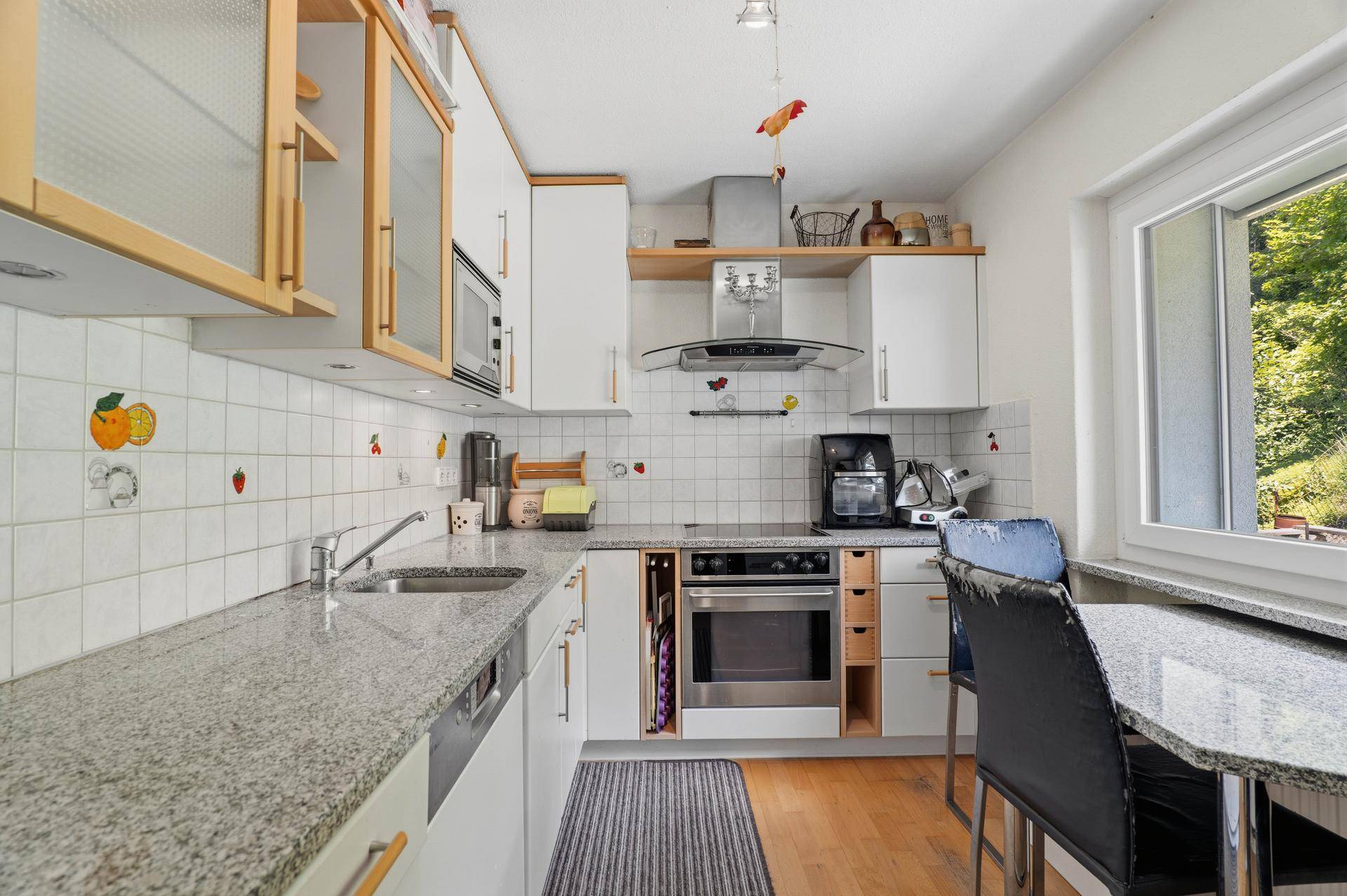 Funktionale Küche mit weißen Schränken, Granitarbeitsplatte und Essbereich am Fenster.