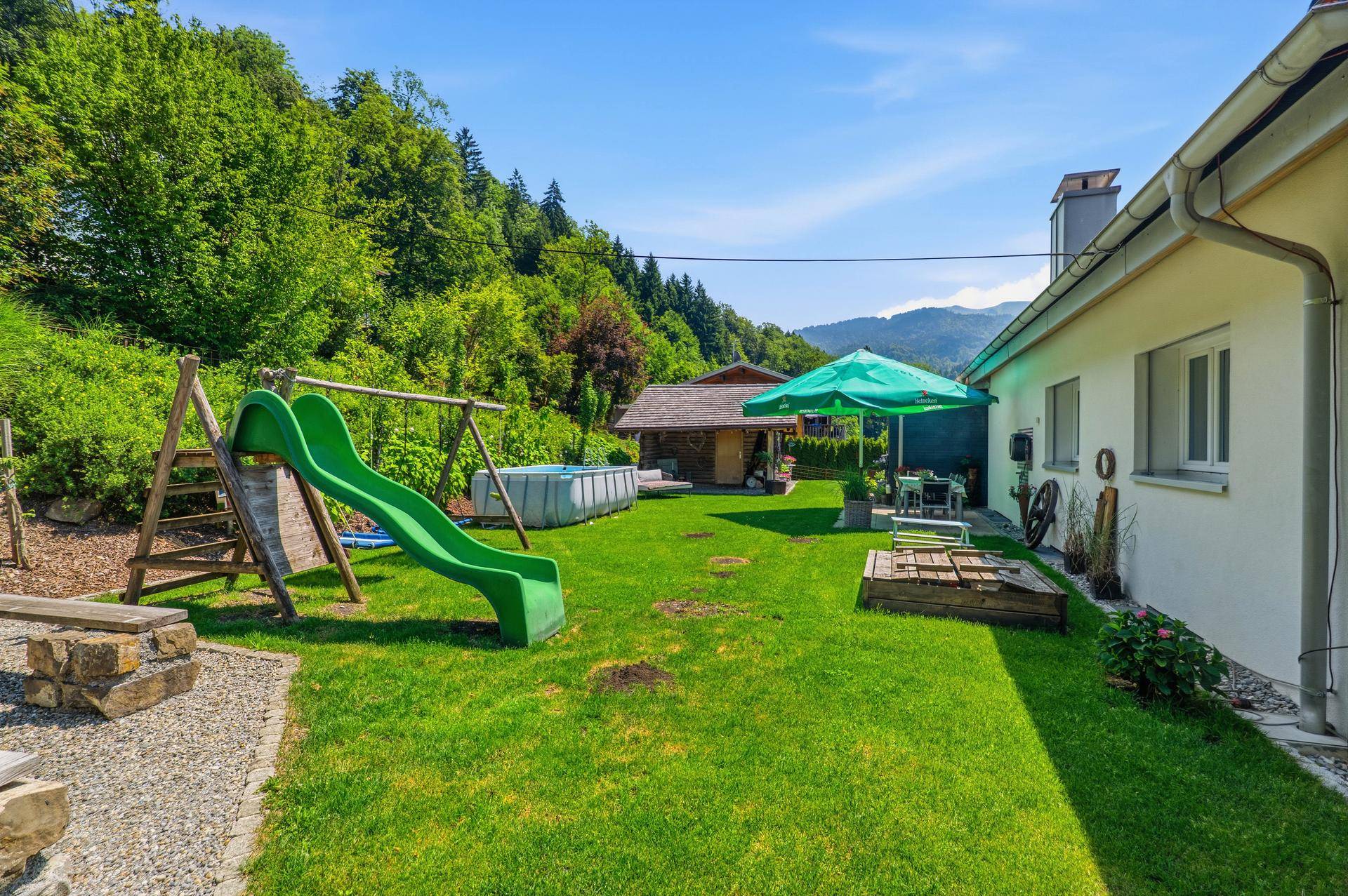 Grüner Garten mit Spielplatz, Pool und Sitzbereich im Freien.