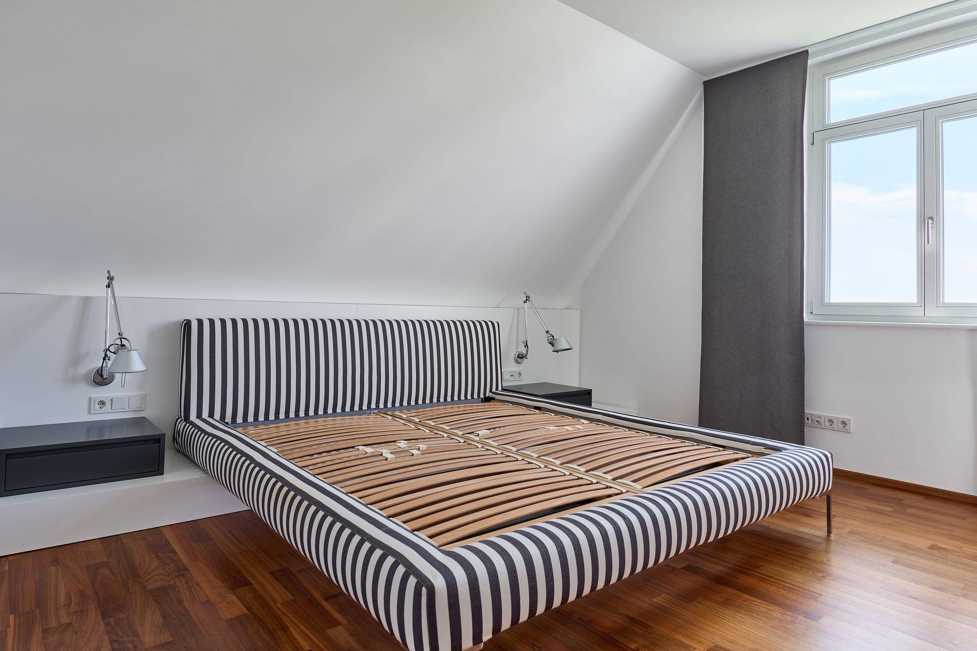 Schlafzimmer im Dachgeschoss mit Holzboden, schrägen Wänden und einem auffälligen gestreiften Bettrahmen.