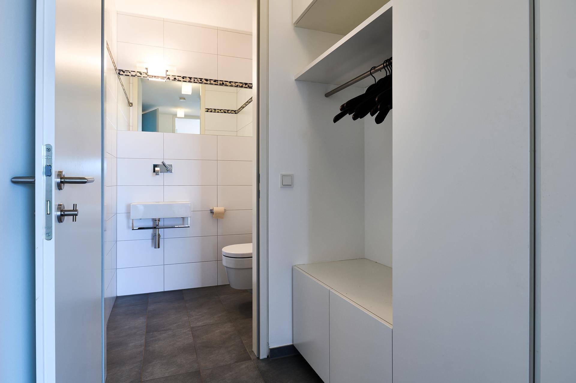 Kleines Gäste-WC mit weißen Fliesen und einem praktischen offenen Stauraum oder Garderobenbereich.