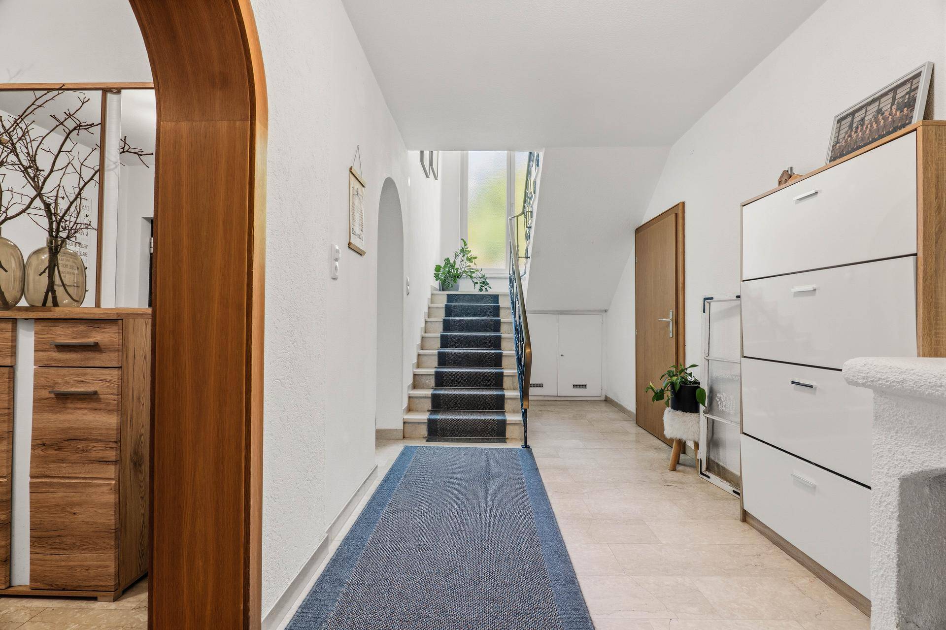 Heller Flur mit Treppenaufgang, Fliesenboden und Holzdetails.