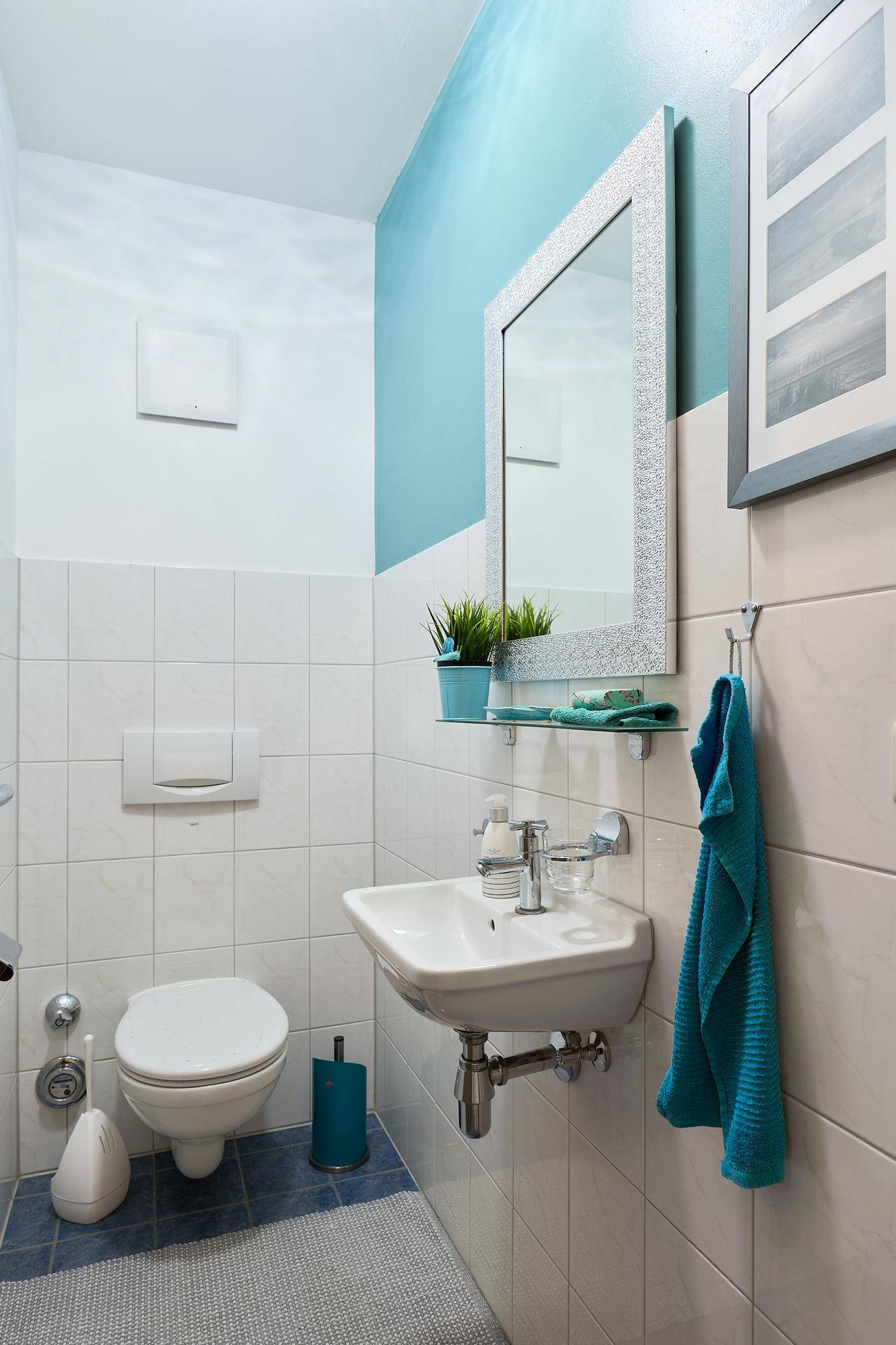 Modernes Gäste-WC mit Wand-WC, Waschbecken und einem Spiegel, akzentuiert durch eine blaue Wand.