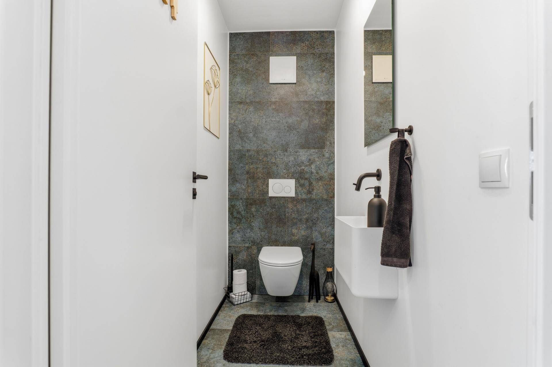 Modernes Gäste-WC mit dunklen Fliesen, Wand-WC und kleinem Waschbecken.