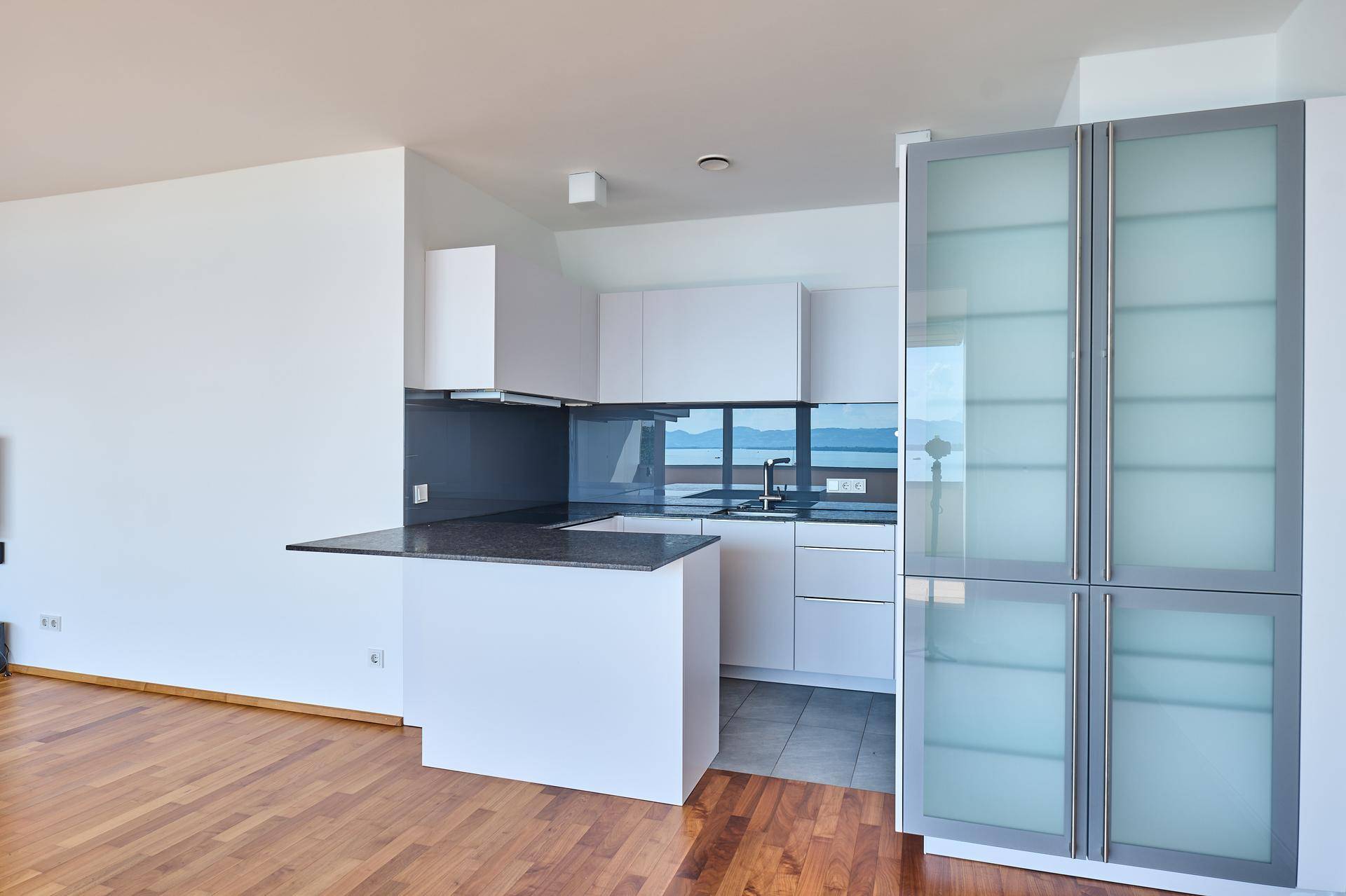 Moderne Einbauküche mit weißen Schränken, dunkler Arbeitsplatte und integrierten Geräten, mit Seeblick.