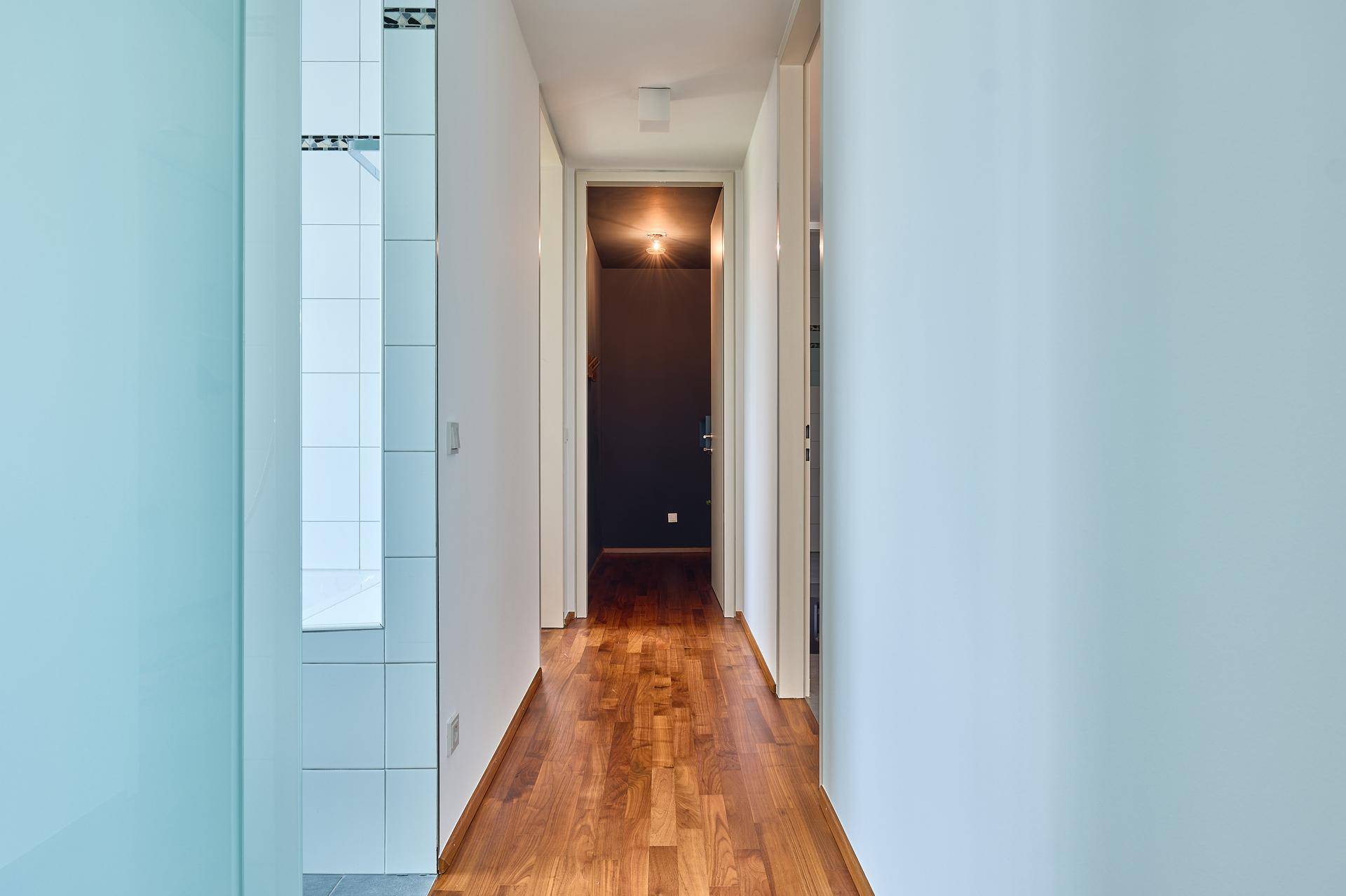 Heller Flur mit Holzboden und weißen Wänden, der zu weiteren Räumen der Wohnung führt.