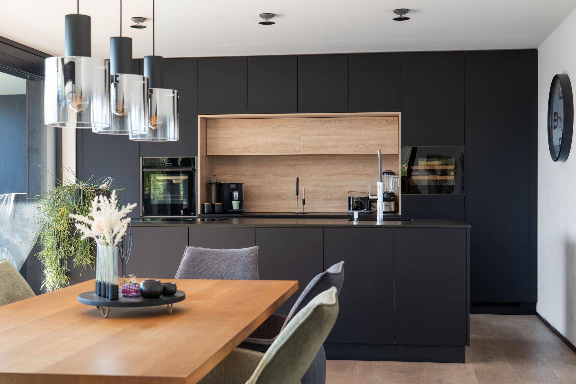 Moderne schwarze Einbauküche mit Holzdetails, integrierten Geräten und Essbereich.