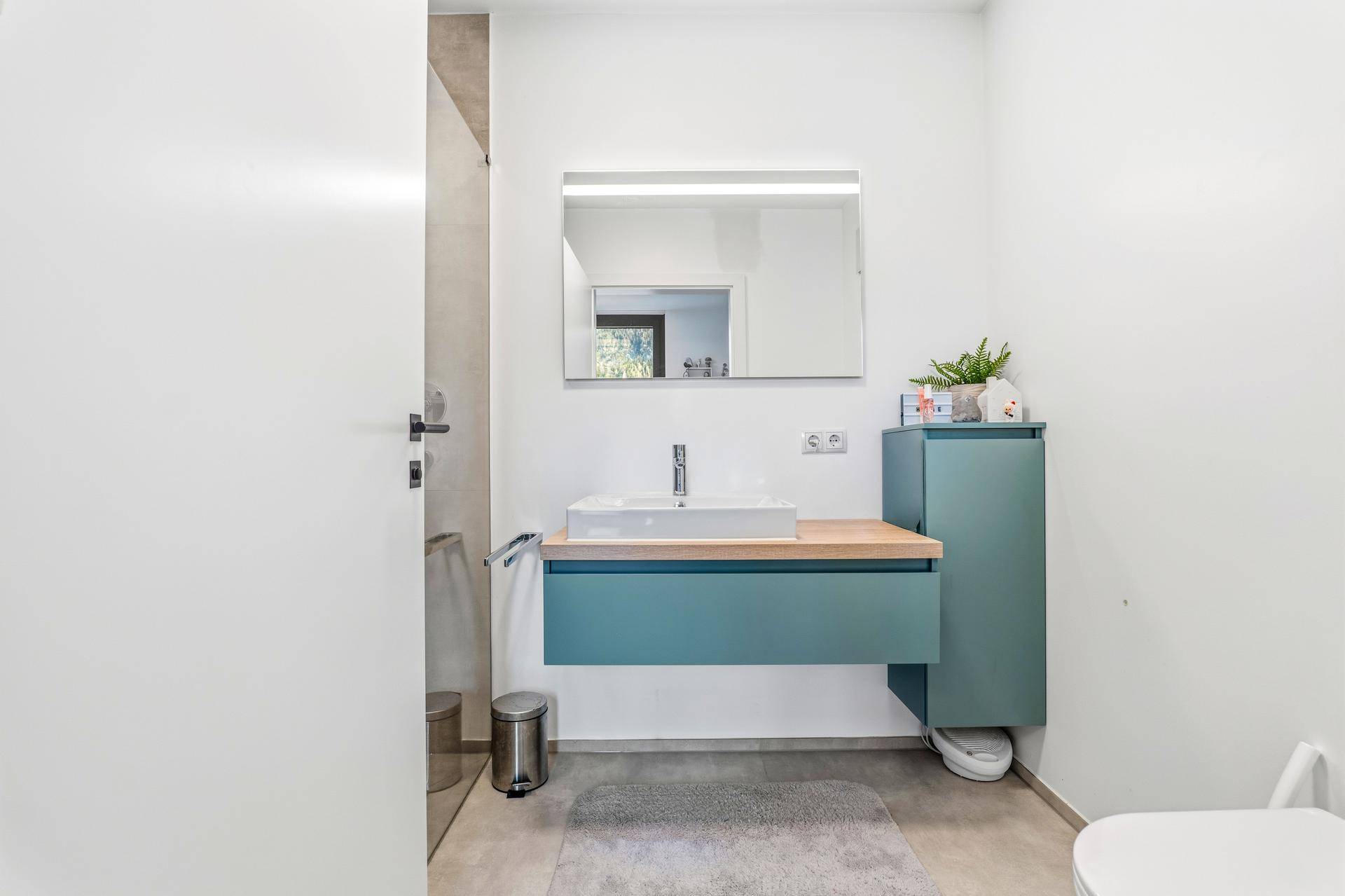 Modernes Badezimmer mit Waschtisch, beleuchtetem Spiegel und Wand-WC.