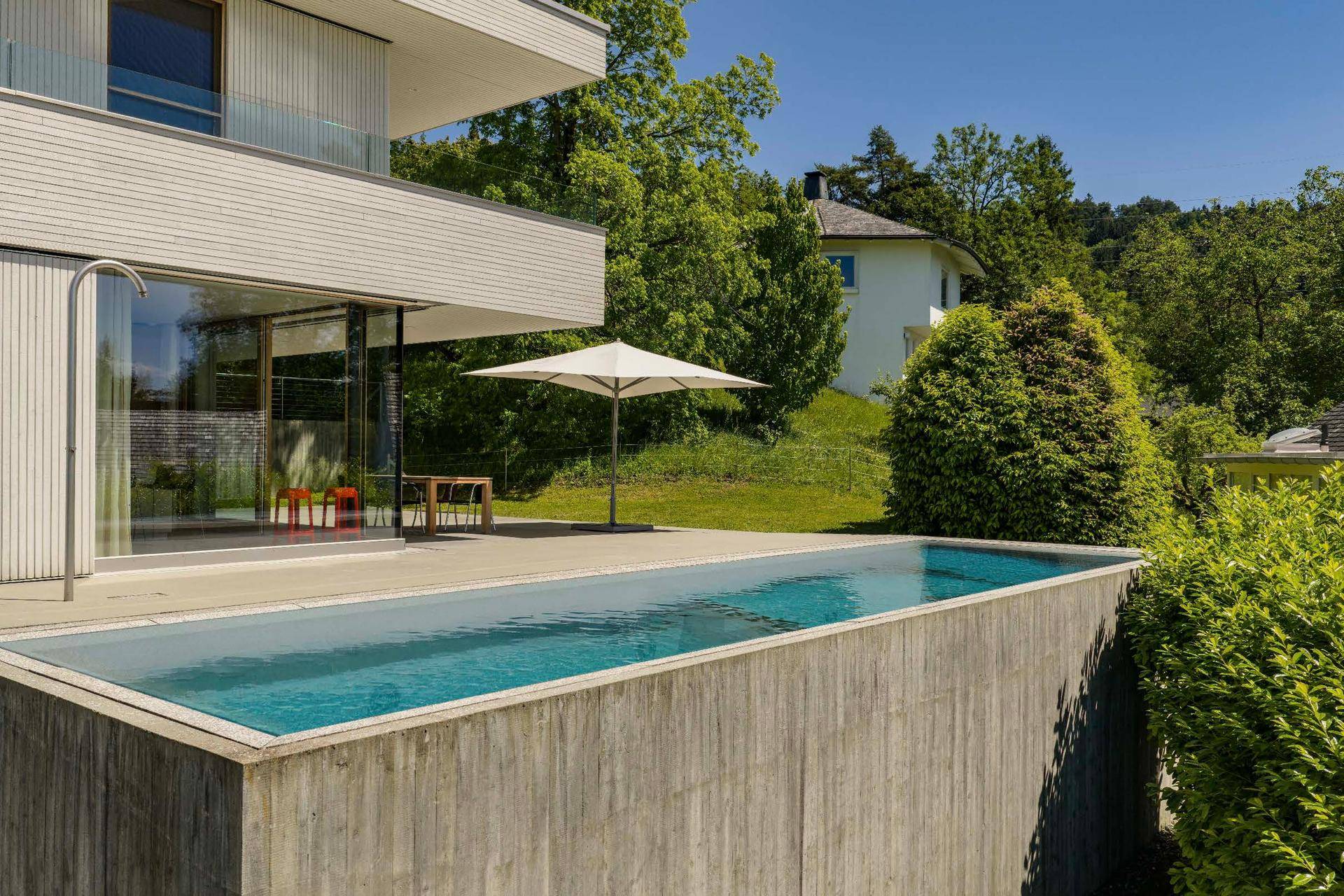 Langer Infinity-Pool neben der modernen Villa, umgeben von Grünflächen und mit weitem Ausblick.
