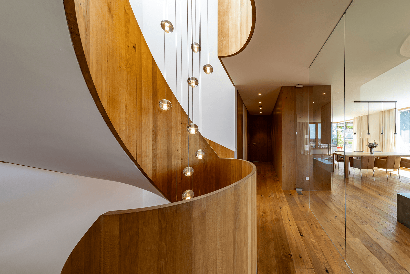 Elegante Holztreppe mit schwebenden Leuchten in einem modernen Flur, der zu einem Essbereich führt.