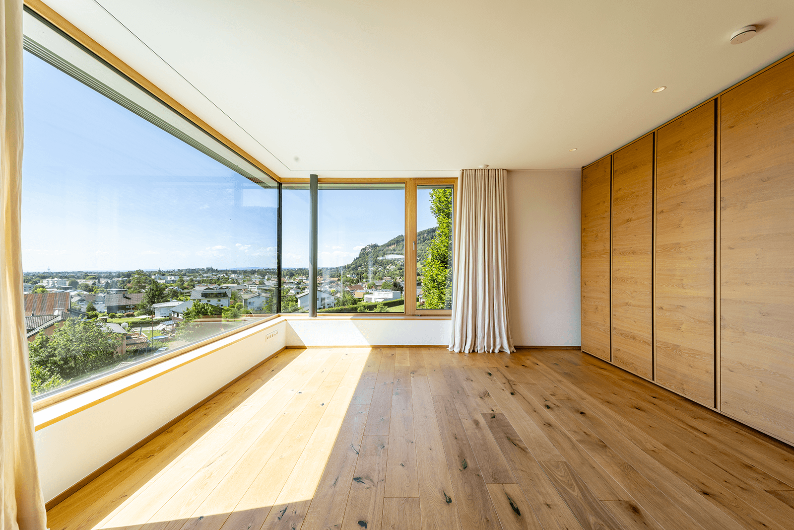 Geräumiges Zimmer mit Holzboden und raumhohen Fenstern, die einen weiten Blick auf die Umgebung bieten.