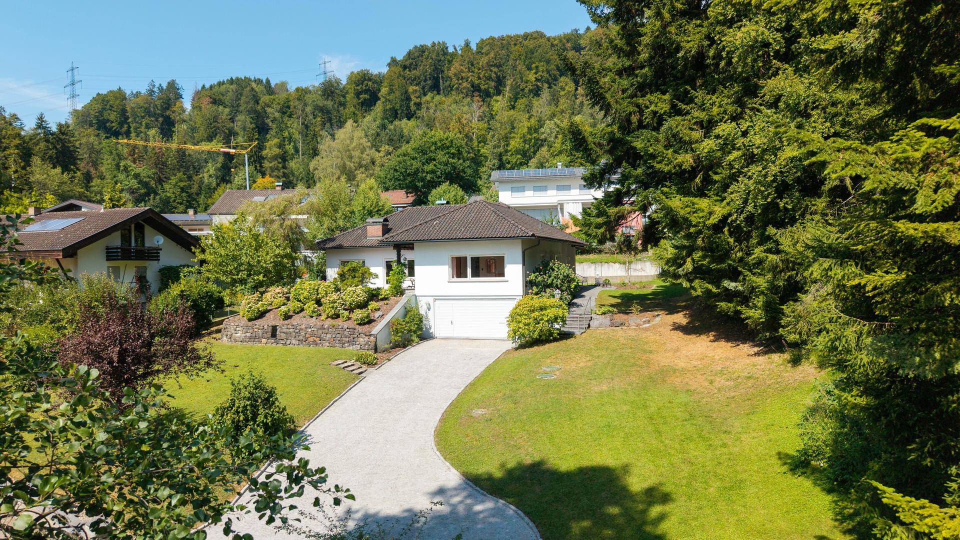Weitläufige Außenansicht des Hauses mit großem Garten, Zufahrt und umgebender Naturlandschaft.