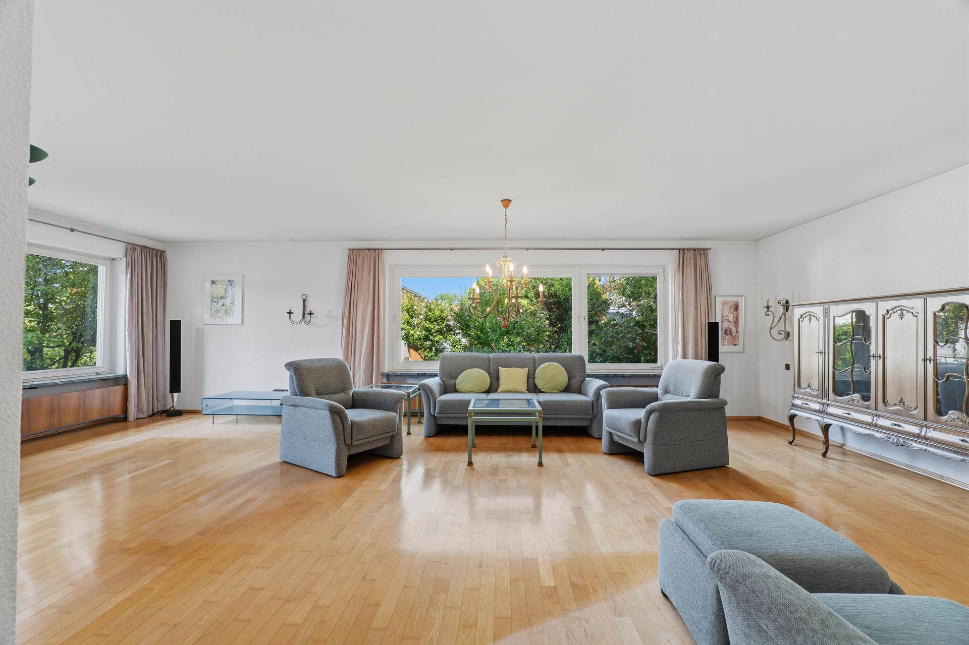 Helles Wohnzimmer mit Holzboden, klassischem Mobiliar und großen Fenstern, die viel Licht hereinlassen.