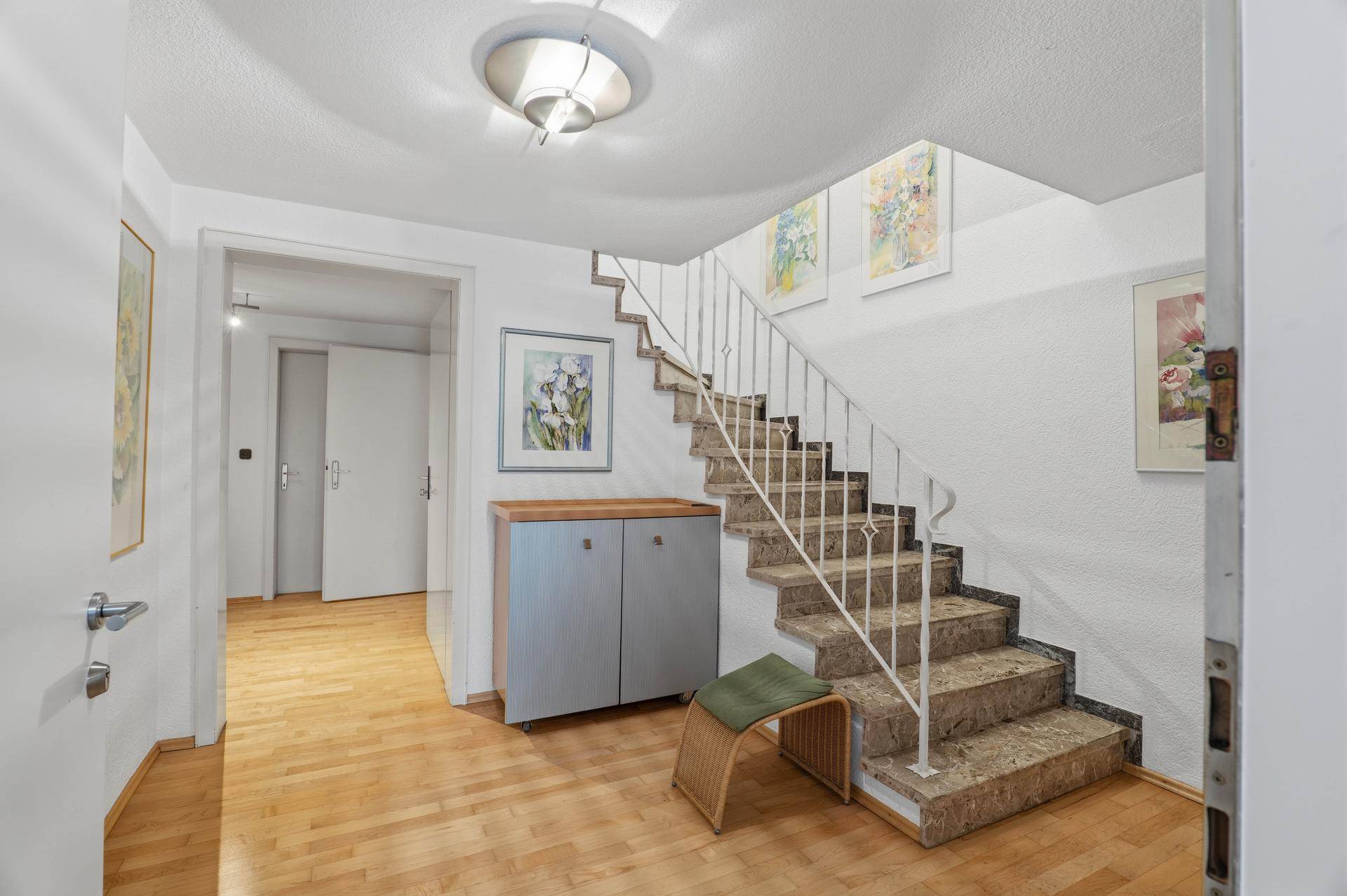 Geräumiger Flur mit Holztreppe, Parkettboden und dekorativen Bildern an den Wänden.