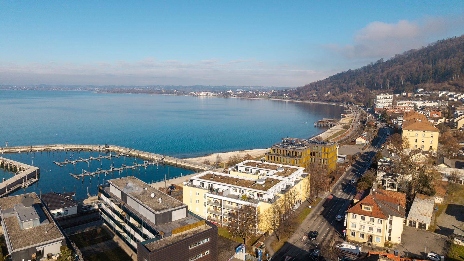 Weitläufiger Blick auf die Küste, den See und die umliegende Bebauung unter blauem Himmel.