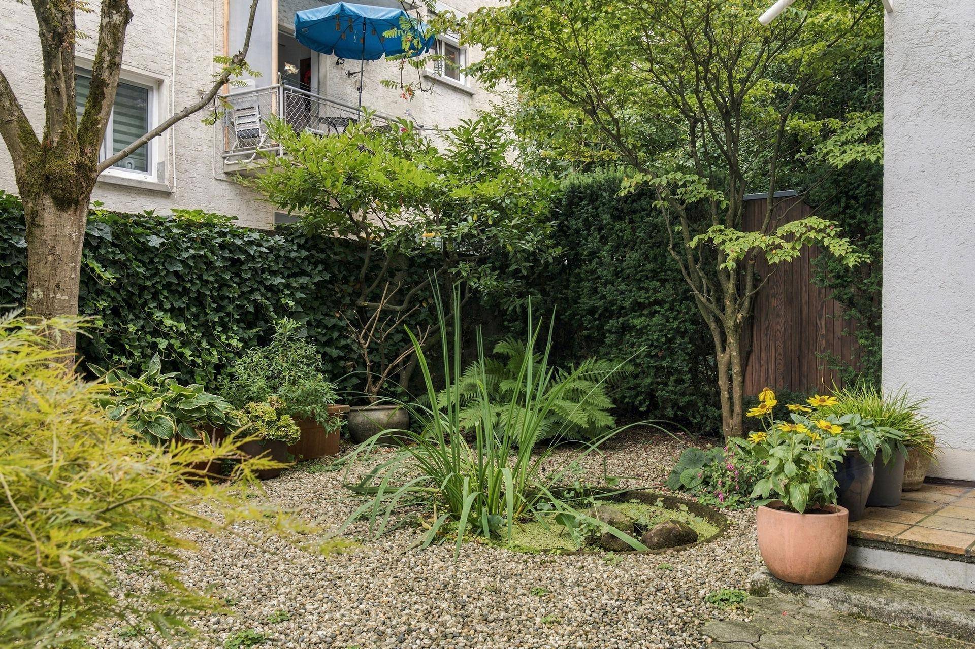 Kleiner, pflegeleichter Gartenbereich mit Zierpflanzen, Kies und einem Teich.