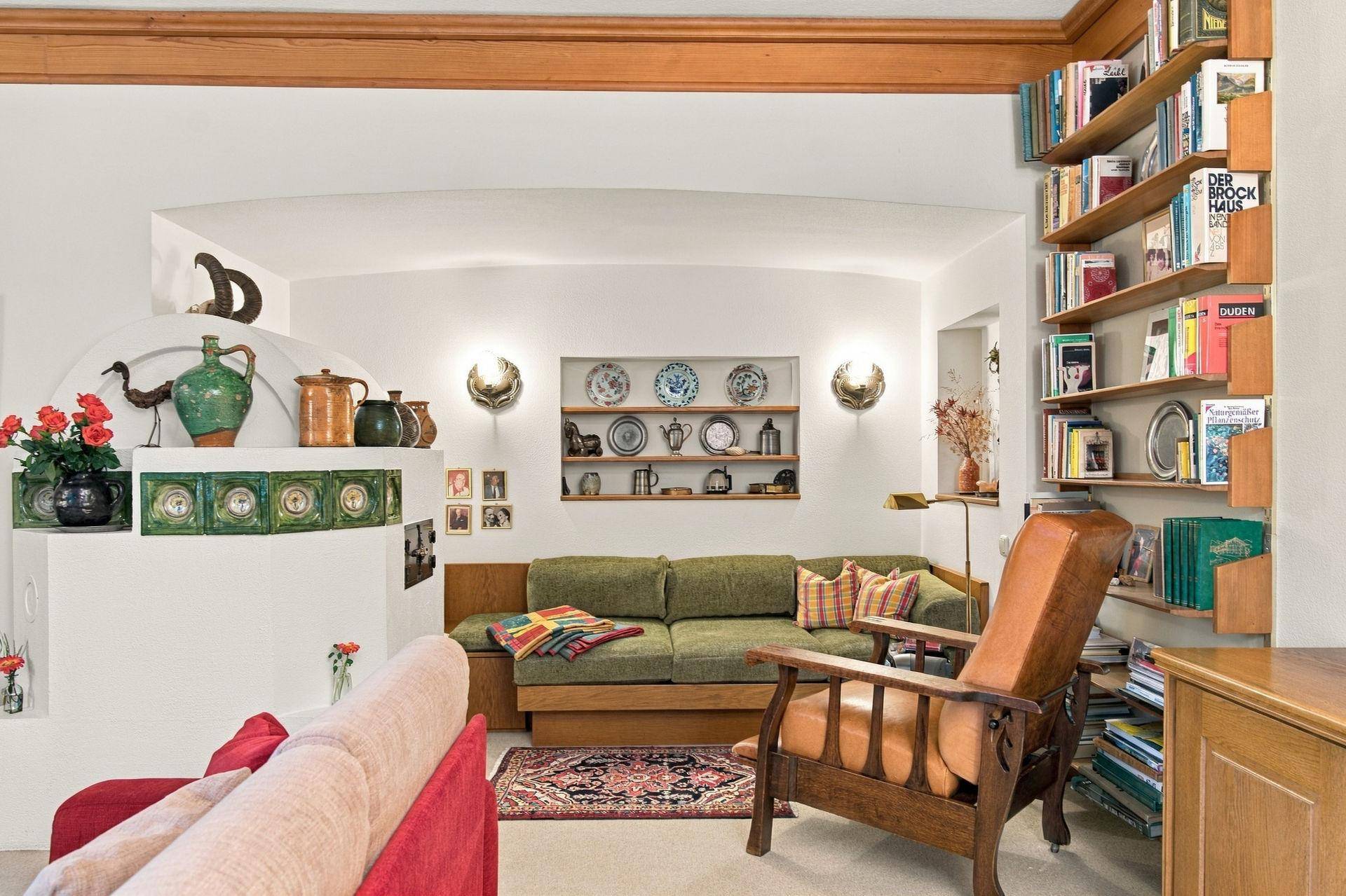Detailansicht eines Wohnbereichs mit grünem Sofa, Kachelofen und dekorativen Wandregalen.