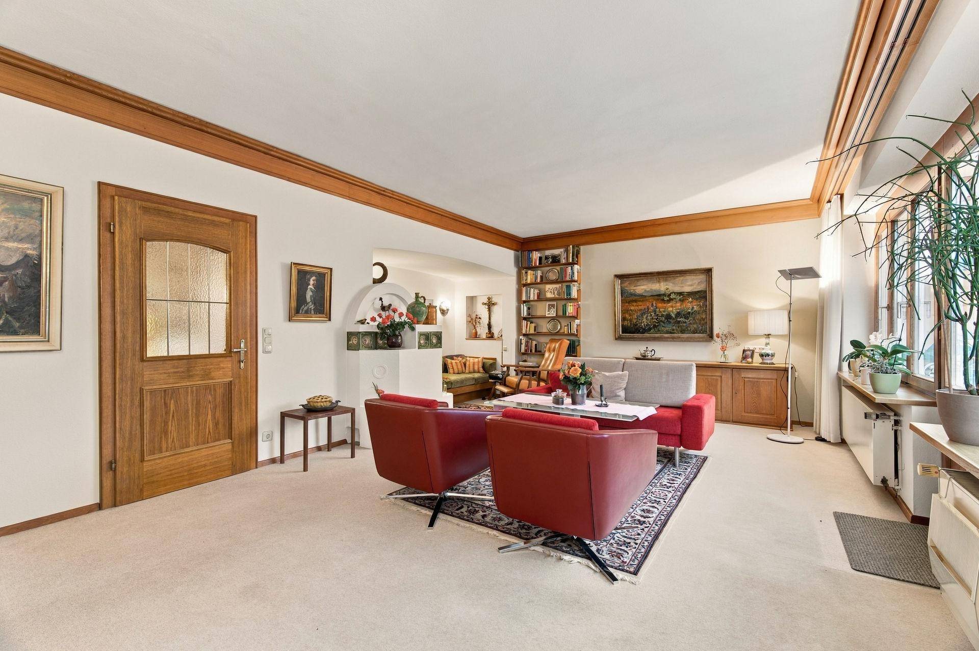 Gemütliches Wohnzimmer mit rotem Sofa, Teppichboden und großen Fenstern.