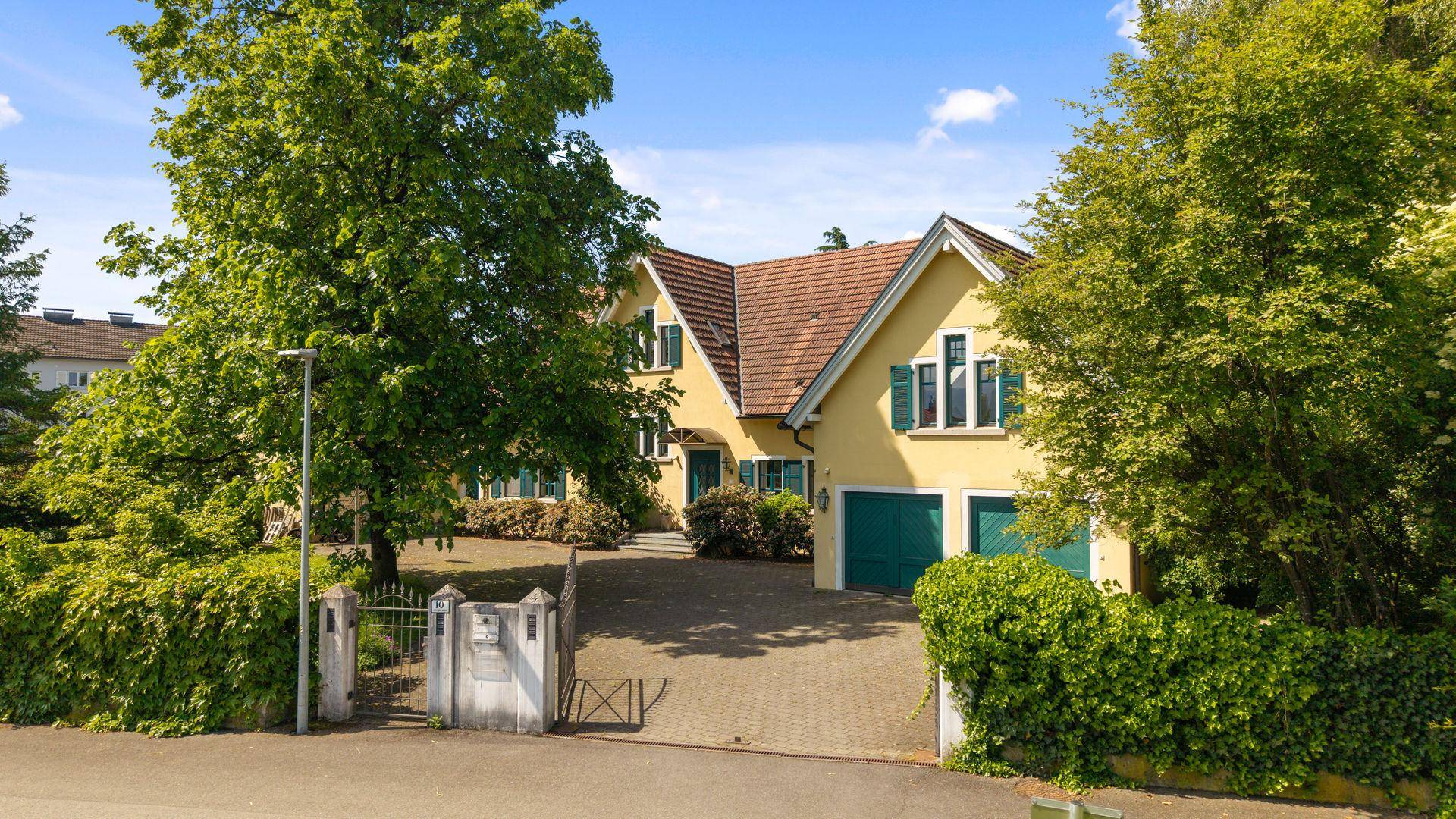 Charmantes Einfamilienhaus mit gelber Fassade, grünen Fensterläden und gepflasterter Auffahrt.