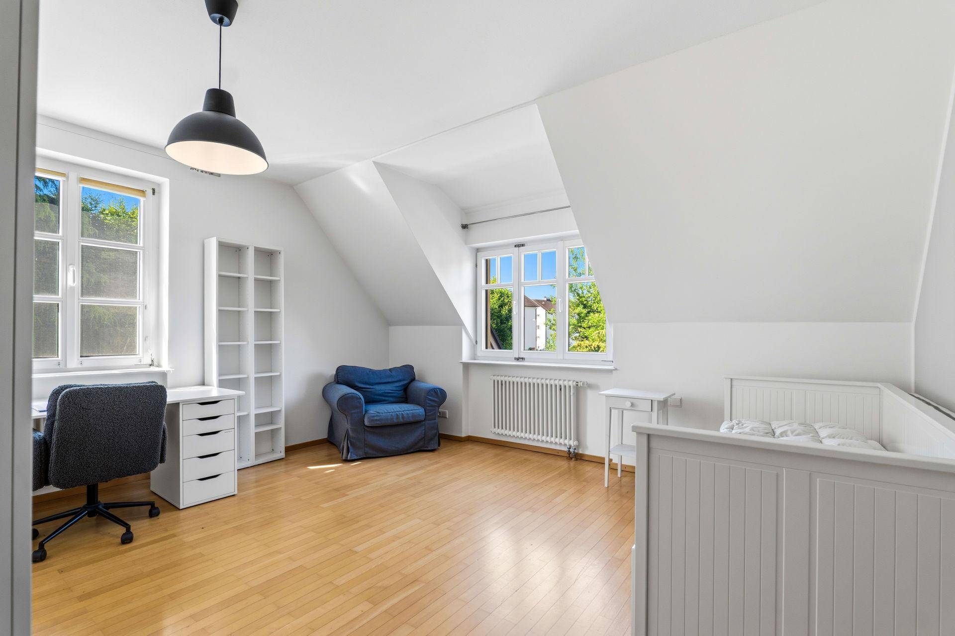 Helles Schlafzimmer mit Holzboden, Schrägdach und Blick ins Grüne, eingerichtet als Kinderzimmer.