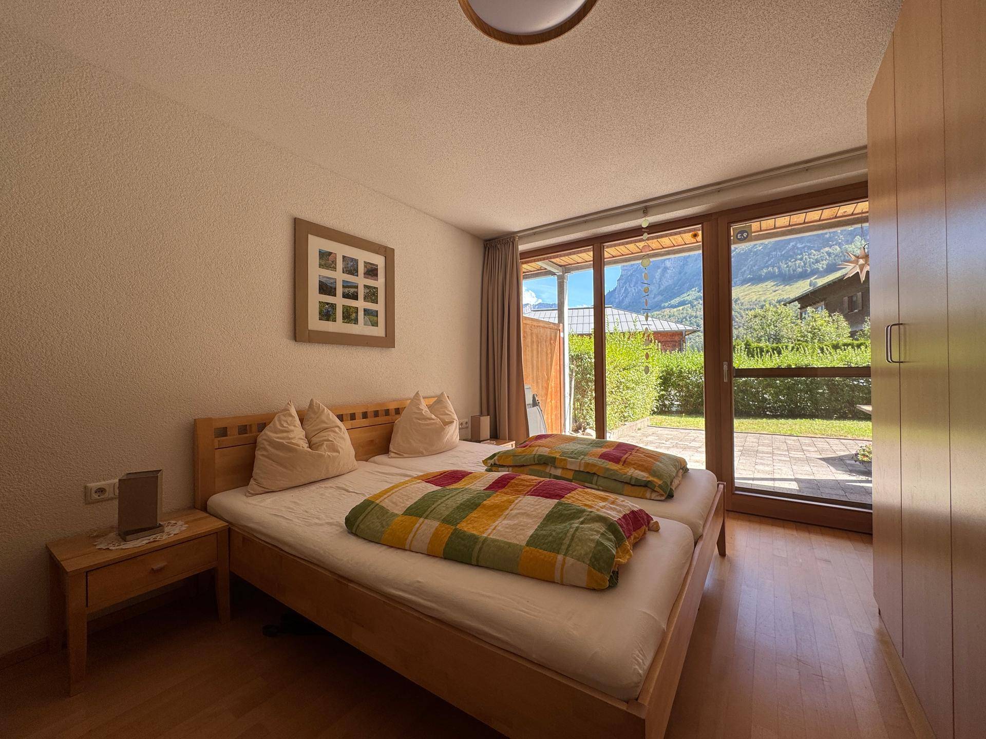 Helles Schlafzimmer mit Doppelbett, Holzmöbeln und direktem Zugang zu einer Terrasse mit Bergblick.