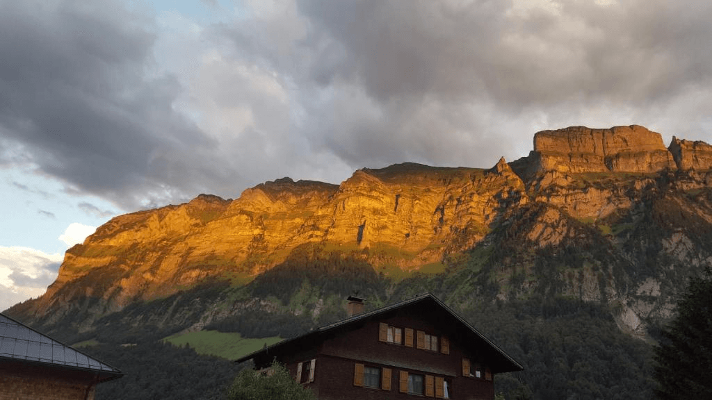Spektakulärer Blick auf die Berge im Abendlicht, mit einem traditionellen Hausdach im Vordergrund.