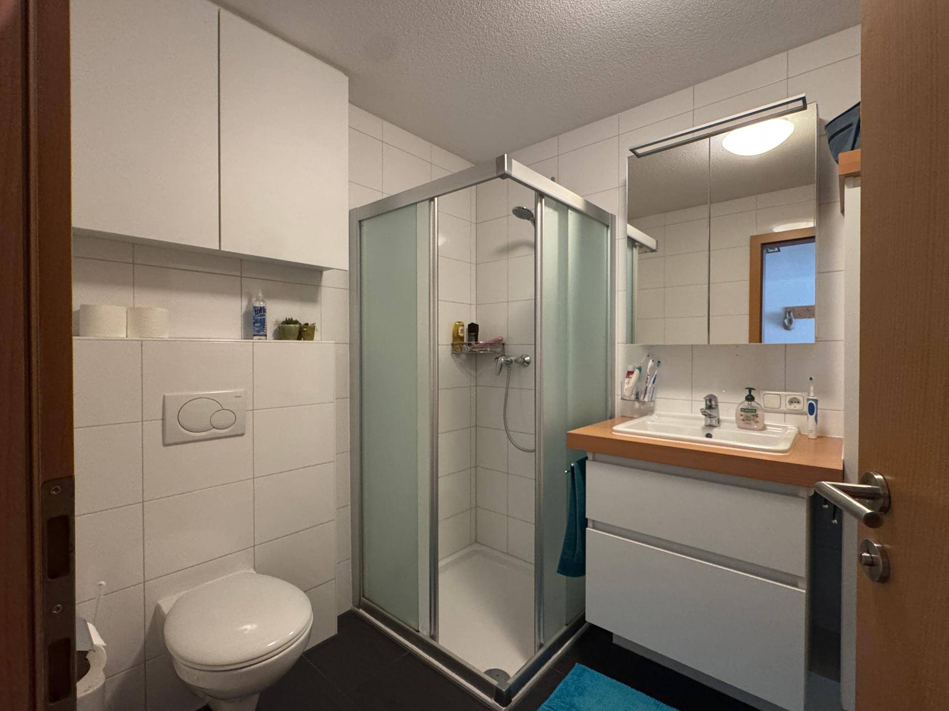 Modernes Badezimmer mit Duschkabine, Toilette und Einzelwaschbecken, hell gefliest.