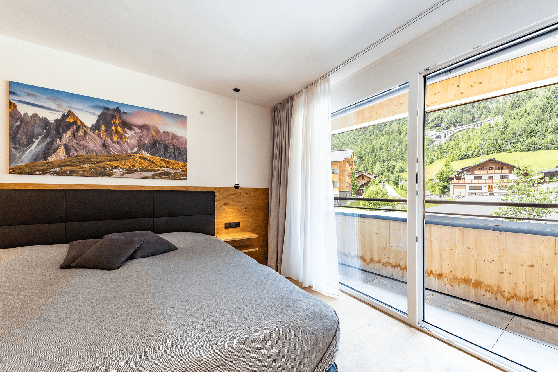 Schlafzimmer mit Balkonzugang, Holzboden und Bergblick, ausgestattet mit einem großen Doppelbett.