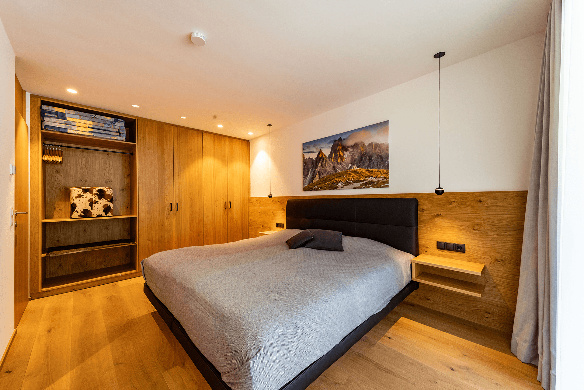 Helles Schlafzimmer mit Holzboden, Einbauschränken und einem großen Bett mit Holzkopfteil.