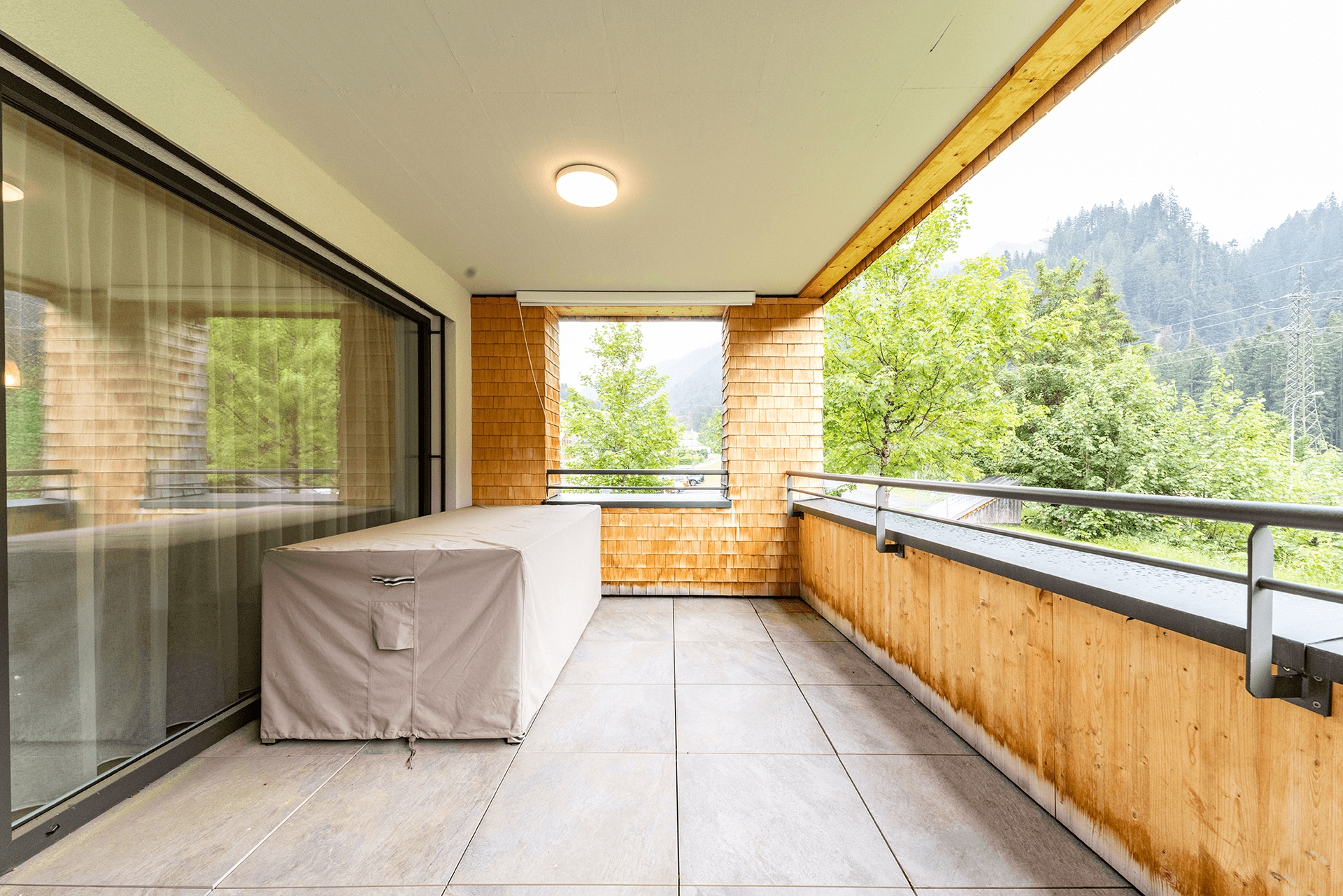Geräumiger Balkon mit Holzwänden, Fliesenboden und Blick auf die umliegende Berglandschaft.