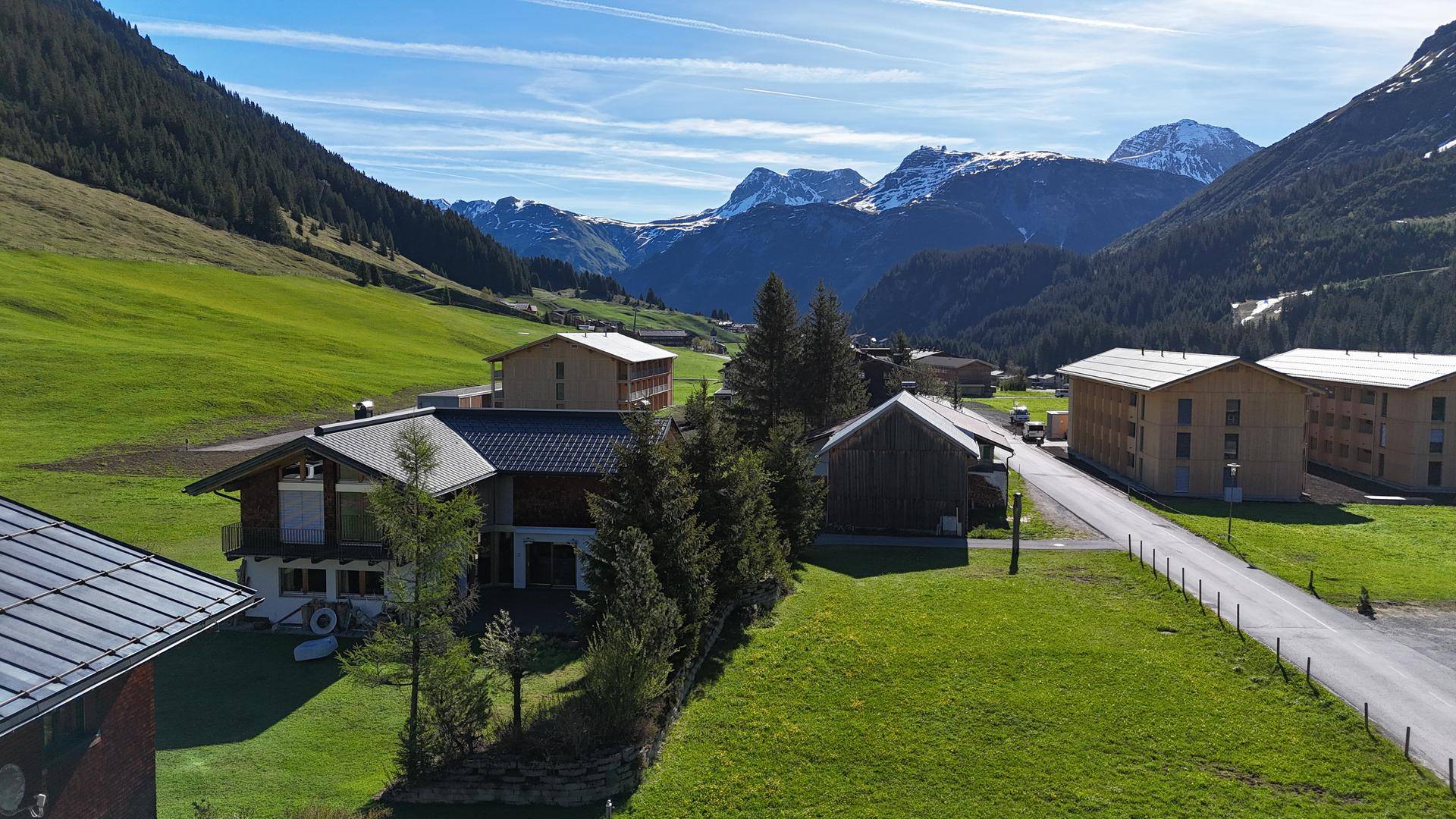 Panoramablick auf traditionelle Häuser in einem Tal mit majestätischen schneebedeckten Bergen im Hintergrund.