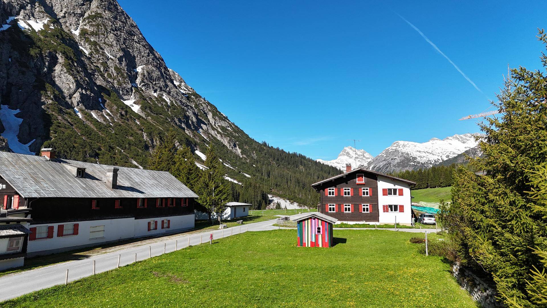 Zwei traditionelle Häuser in einer grünen Landschaft mit imposanten Bergen und klarem blauem Himmel.