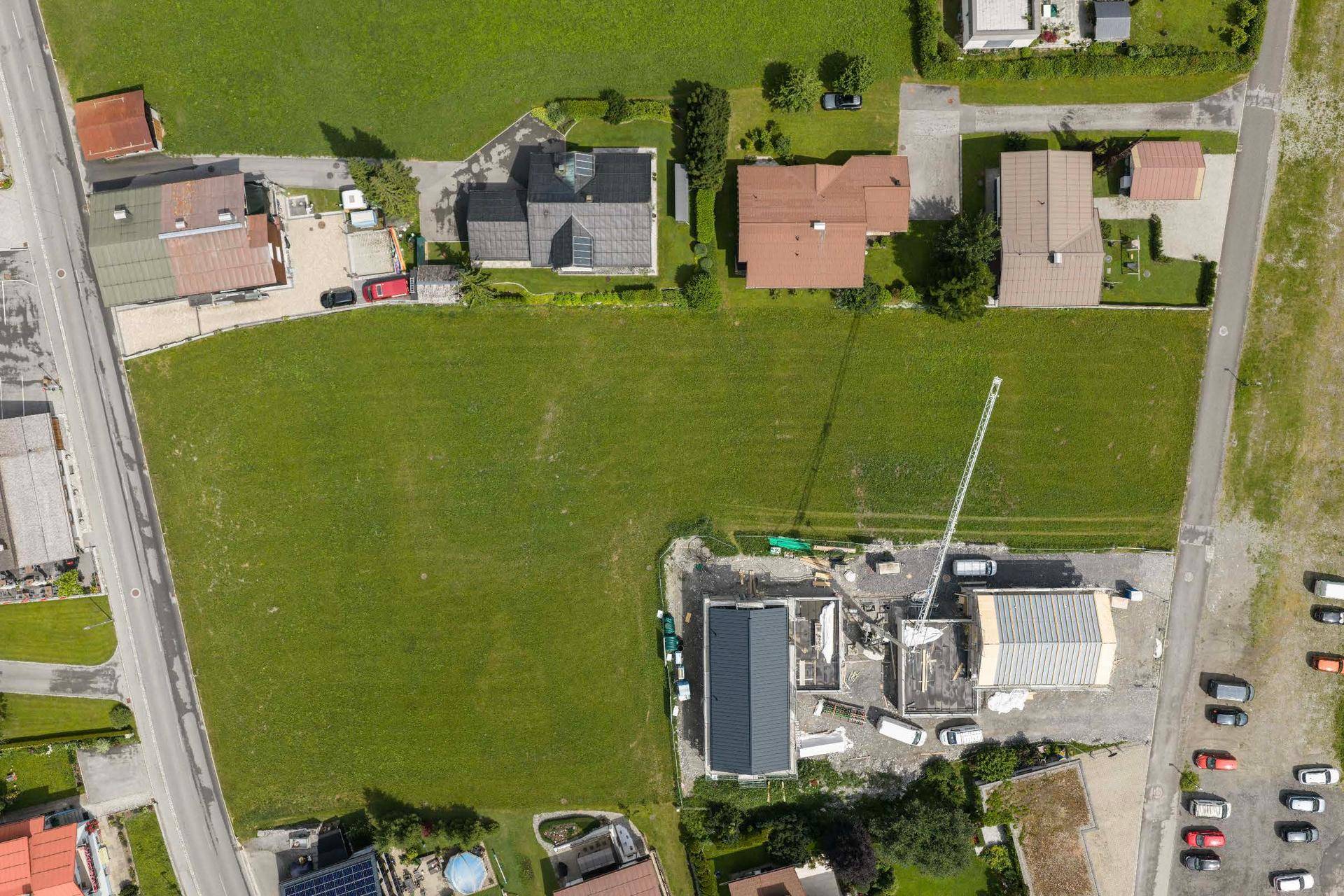 Senkrechte Luftaufnahme einer Baustelle mit umliegenden Wohnhäusern und grünen Feldern.