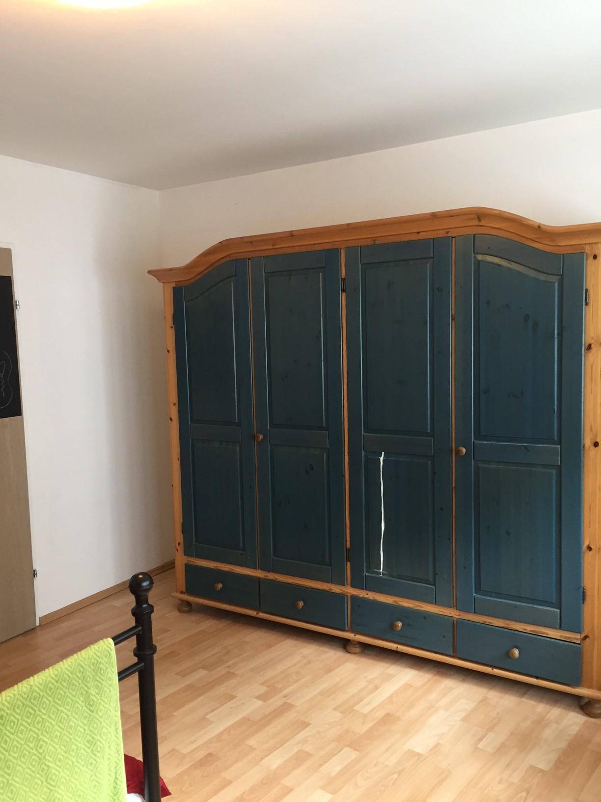 Geräumiges Schlafzimmer mit einem großen blauen Holzschrank und hellem Laminatboden.