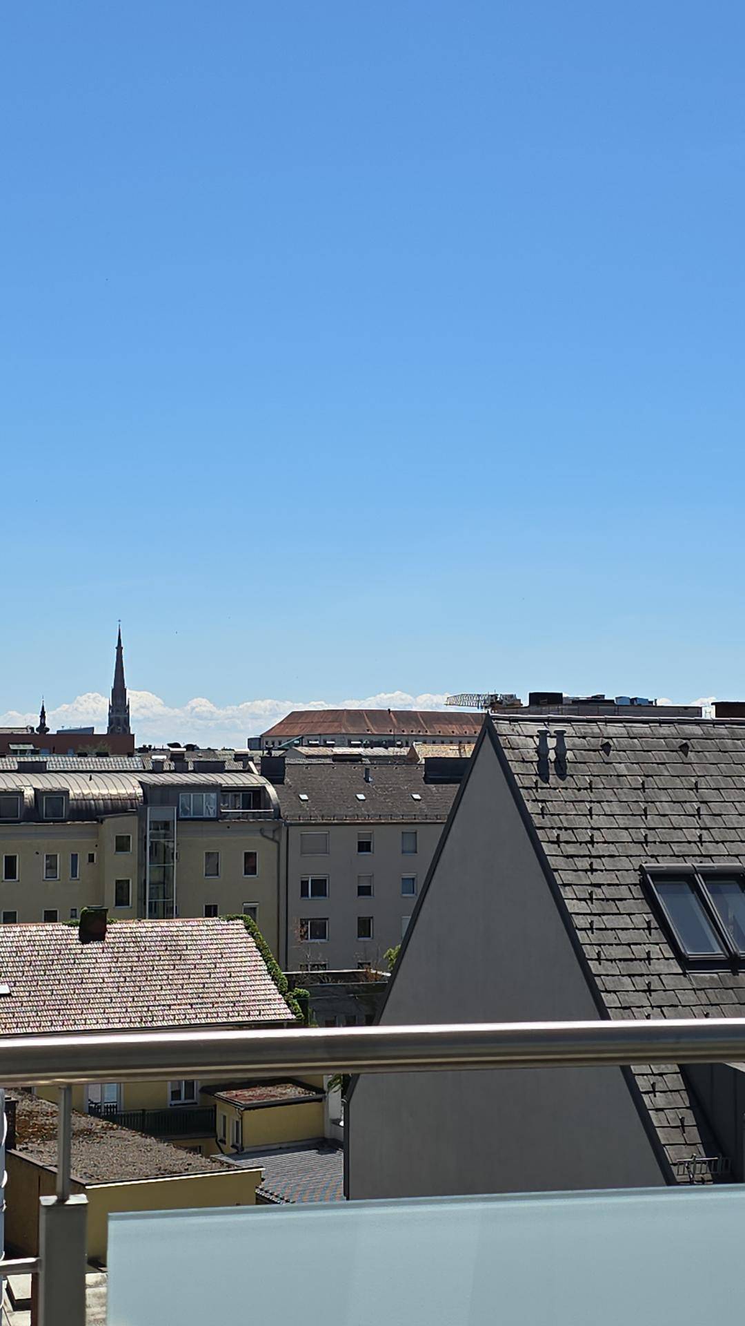Blick von einem Balkon über die Dächer der Stadt an einem sonnigen Tag mit blauem Himmel.