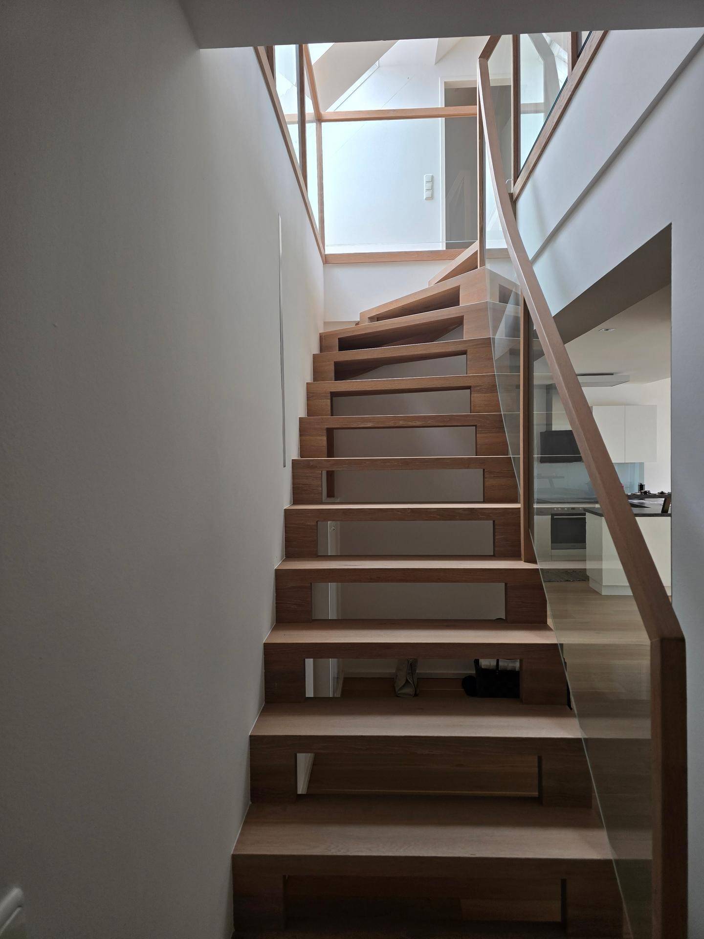 Moderne Holztreppe mit Glasgeländer, die verschiedene Ebenen des Hauses miteinander verbindet.