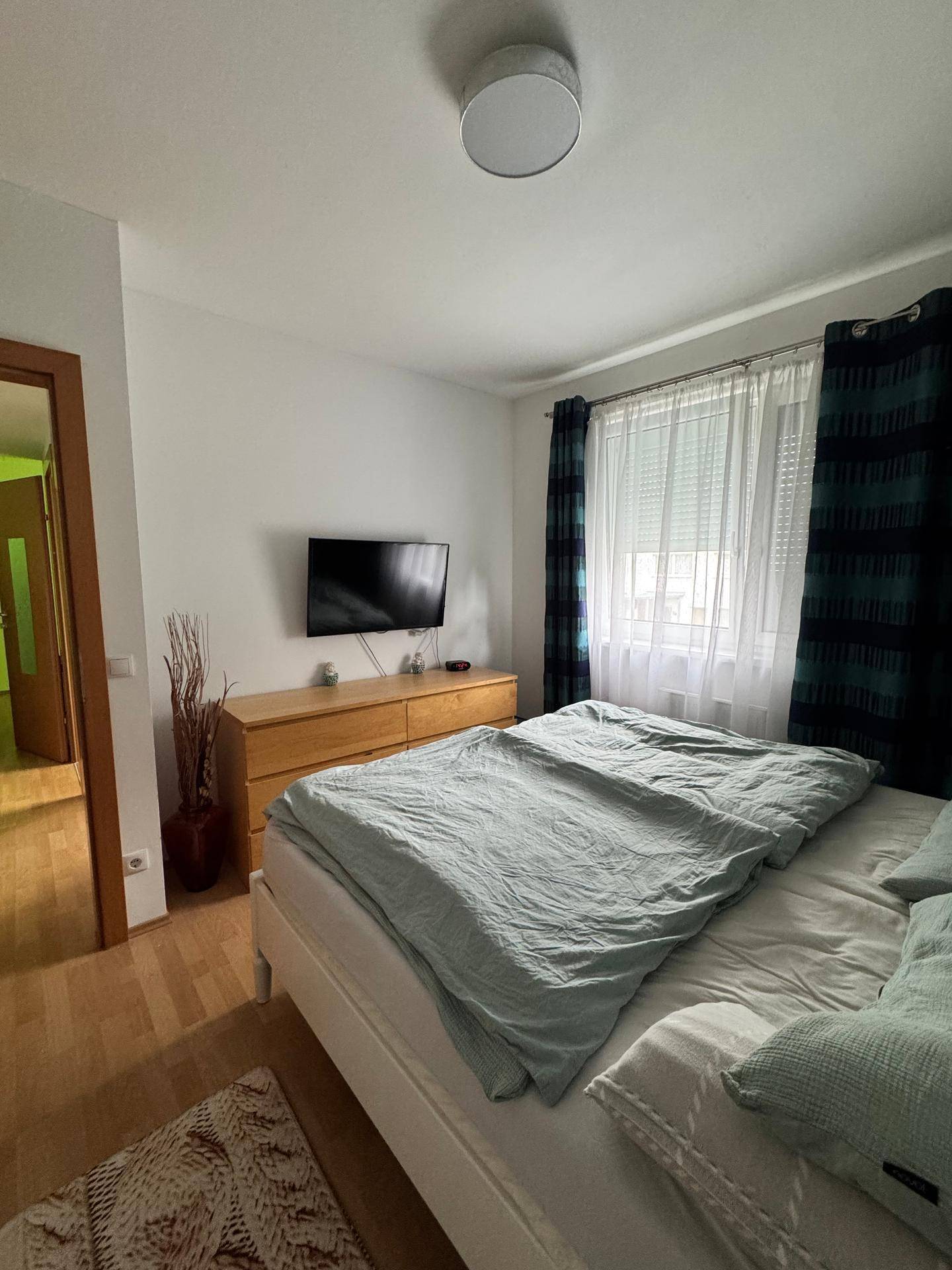 Helles Schlafzimmer mit Doppelbett, Kommode und Wandfernseher, einladend und komfortabel gestaltet.