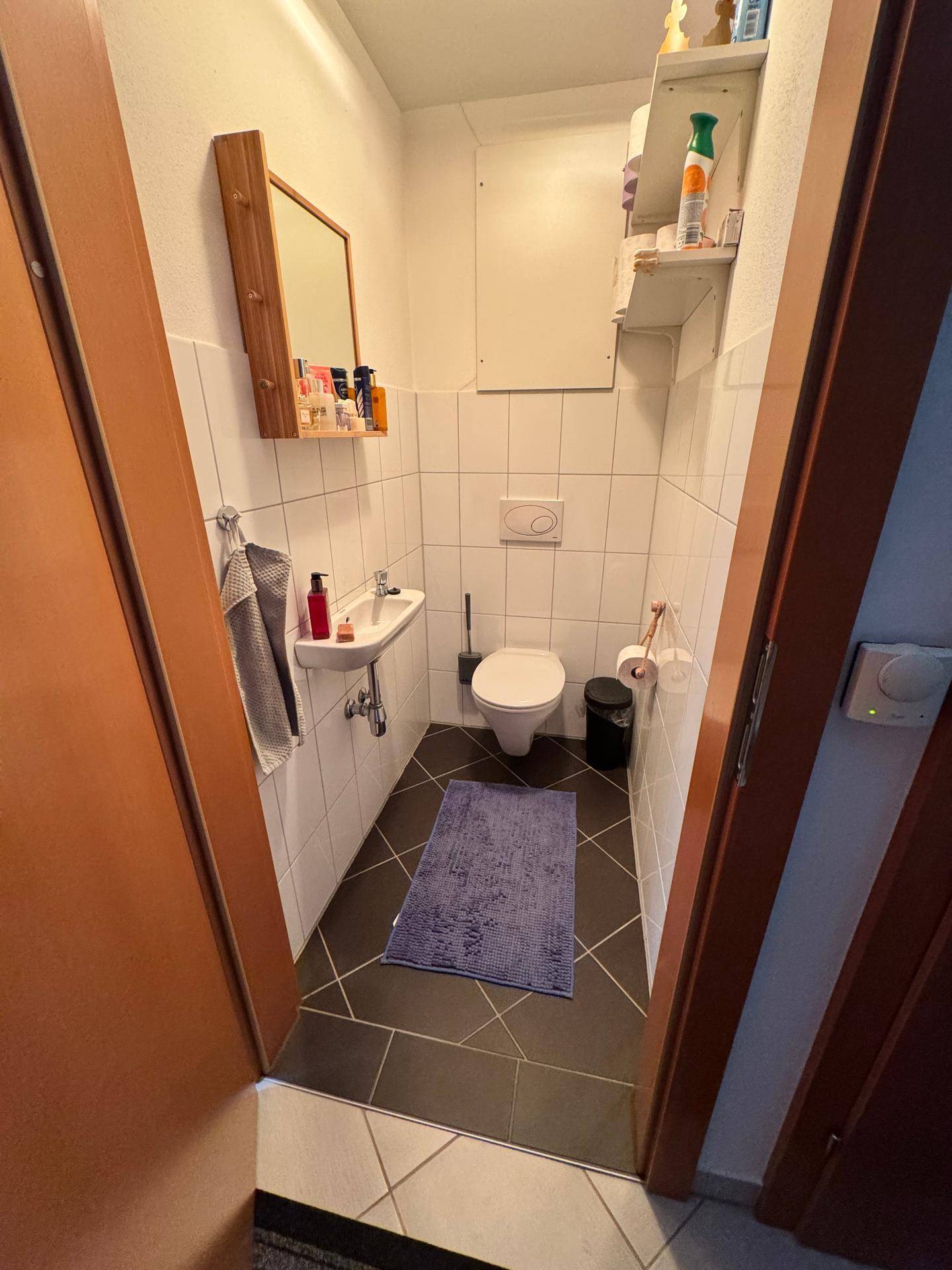 Kleines Gäste-WC mit Wand-WC, Waschbecken und Spiegel, funktional und hell gefliest.