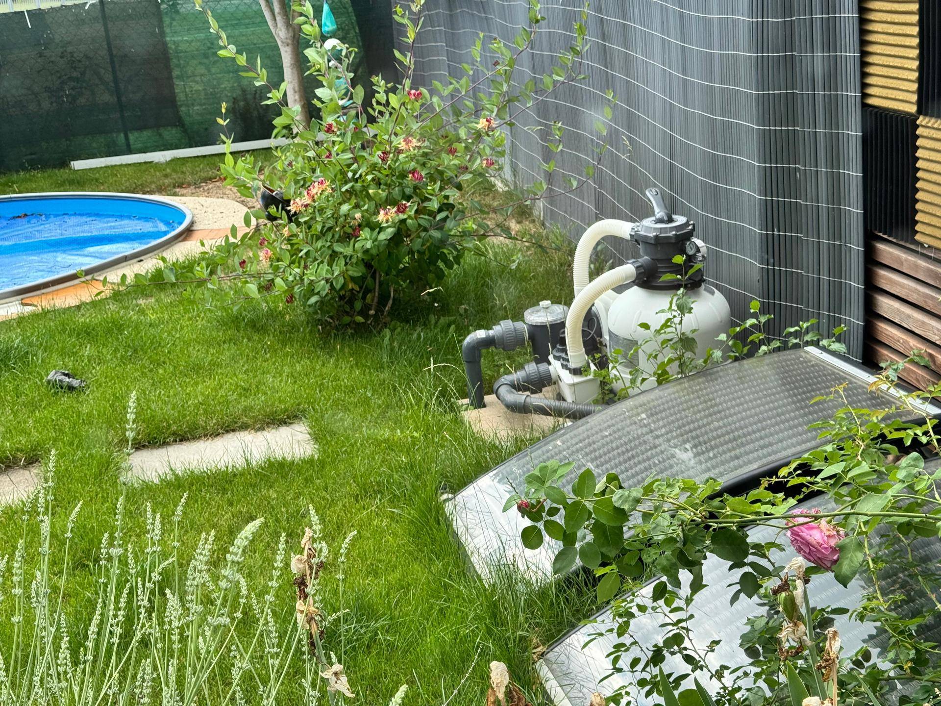 Garten mit Pooltechnik, Solarpaneelen und blühenden Pflanzen, umgeben von Grünflächen.