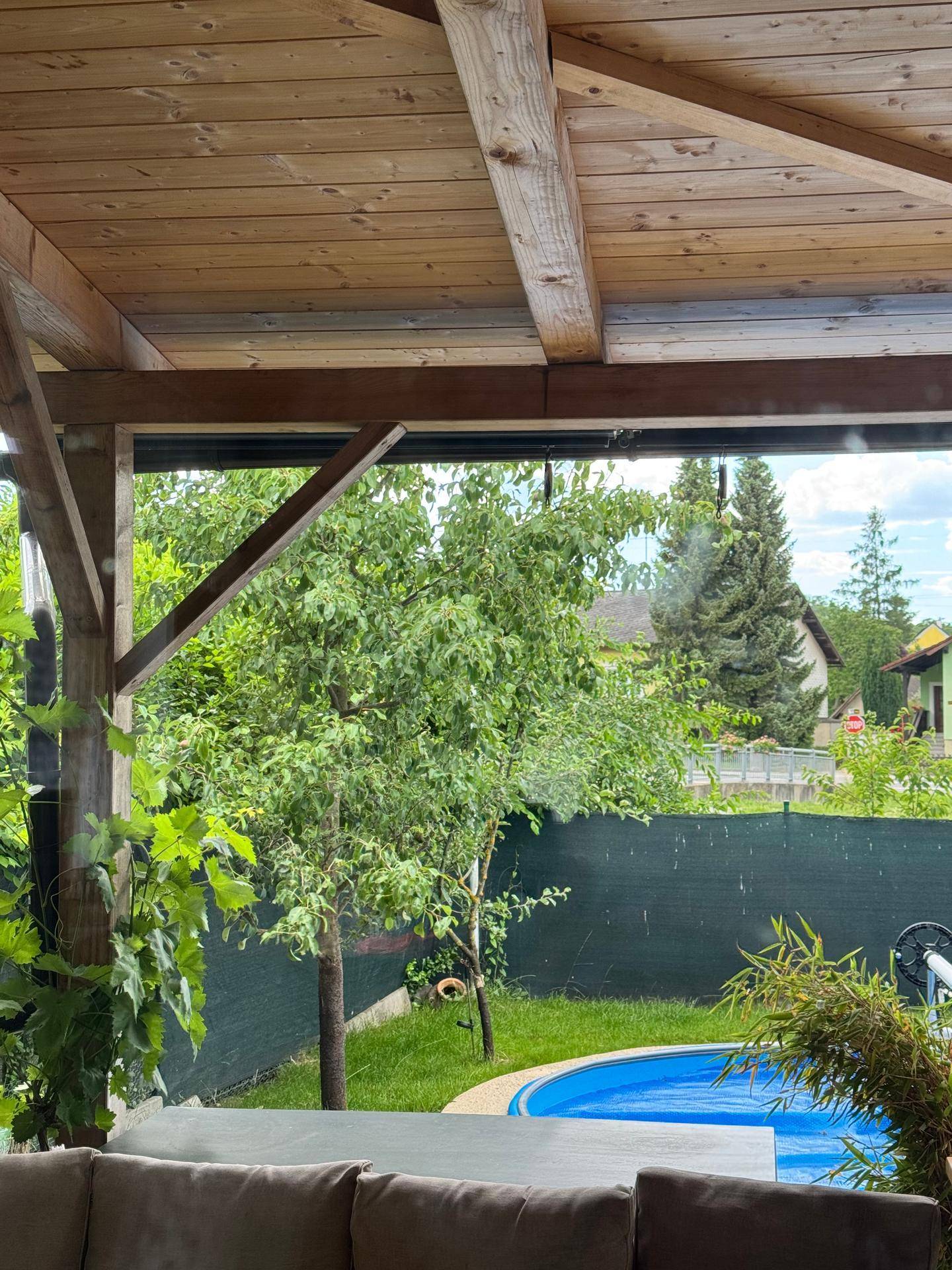 Blick vom überdachten Außenbereich auf den Garten mit Pool und üppiger Vegetation.