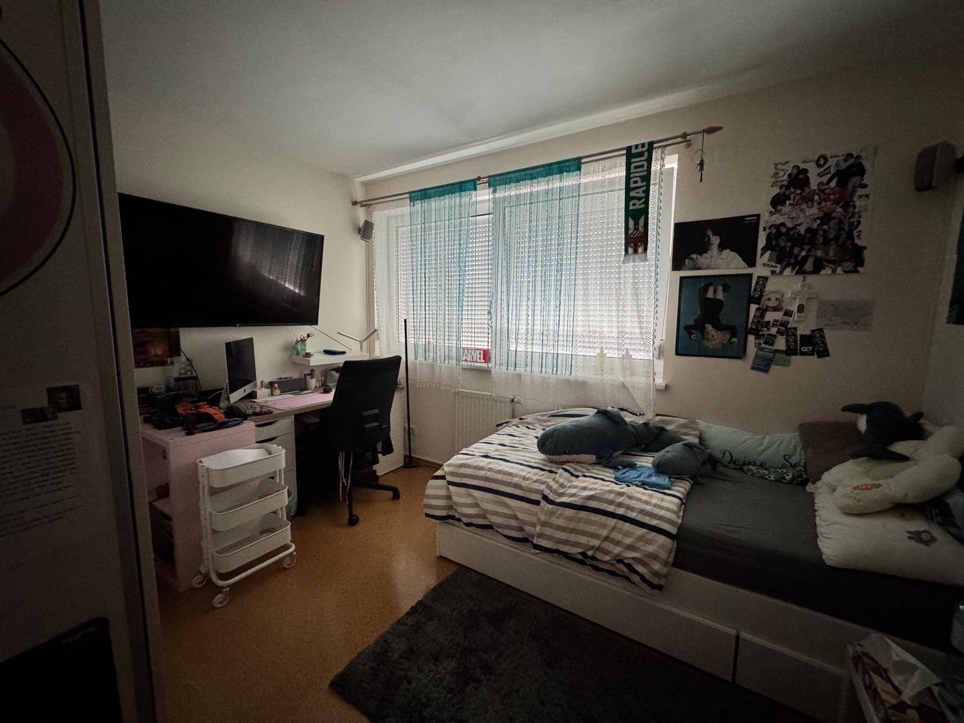 Jugendzimmer mit Bett, Schreibtisch und Fernseher am Fenster, funktional und persönlich eingerichtet.