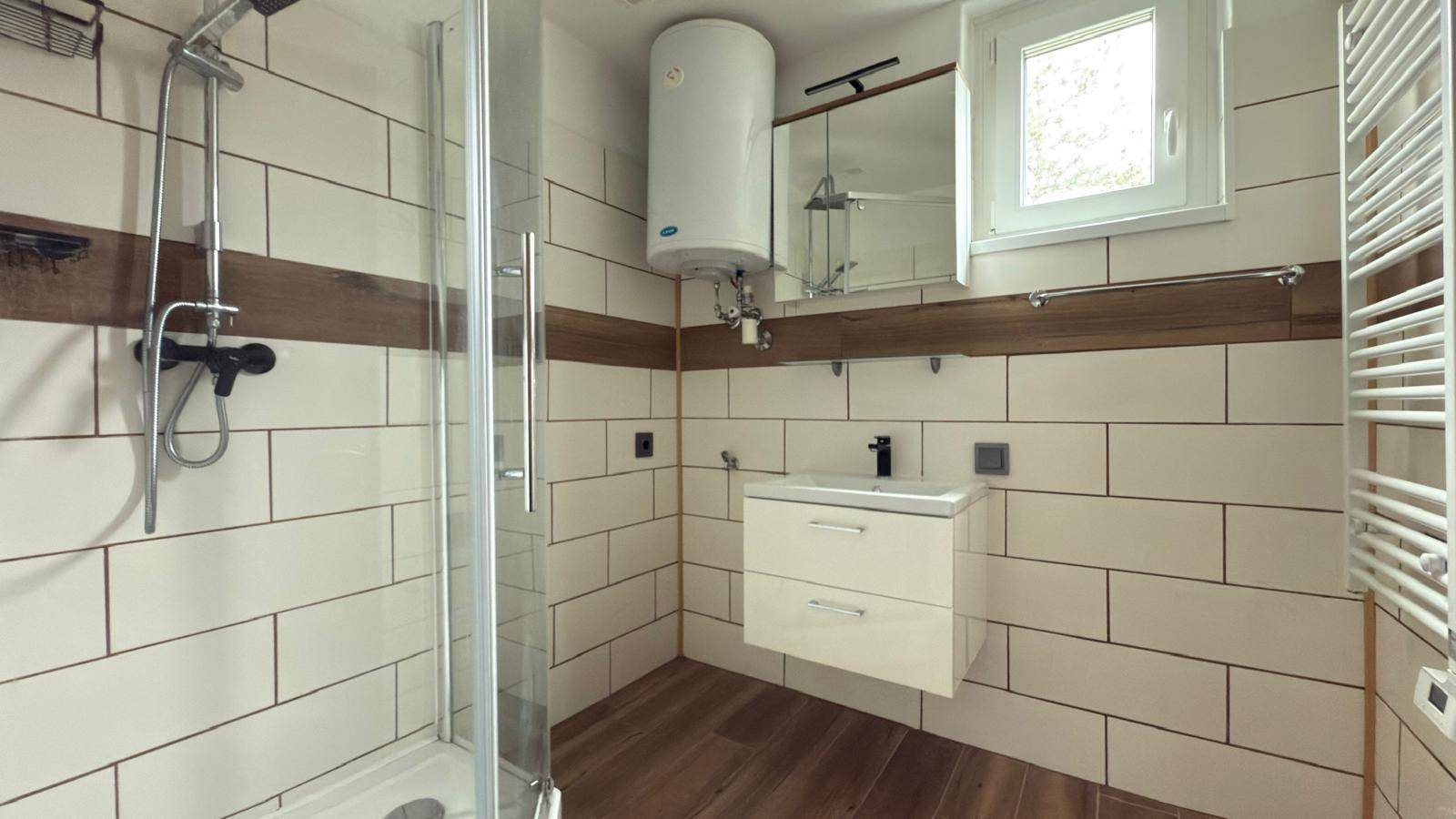 Modernes Badezimmer mit Duschkabine, Waschbecken, Fenster und beheiztem Handtuchhalter.