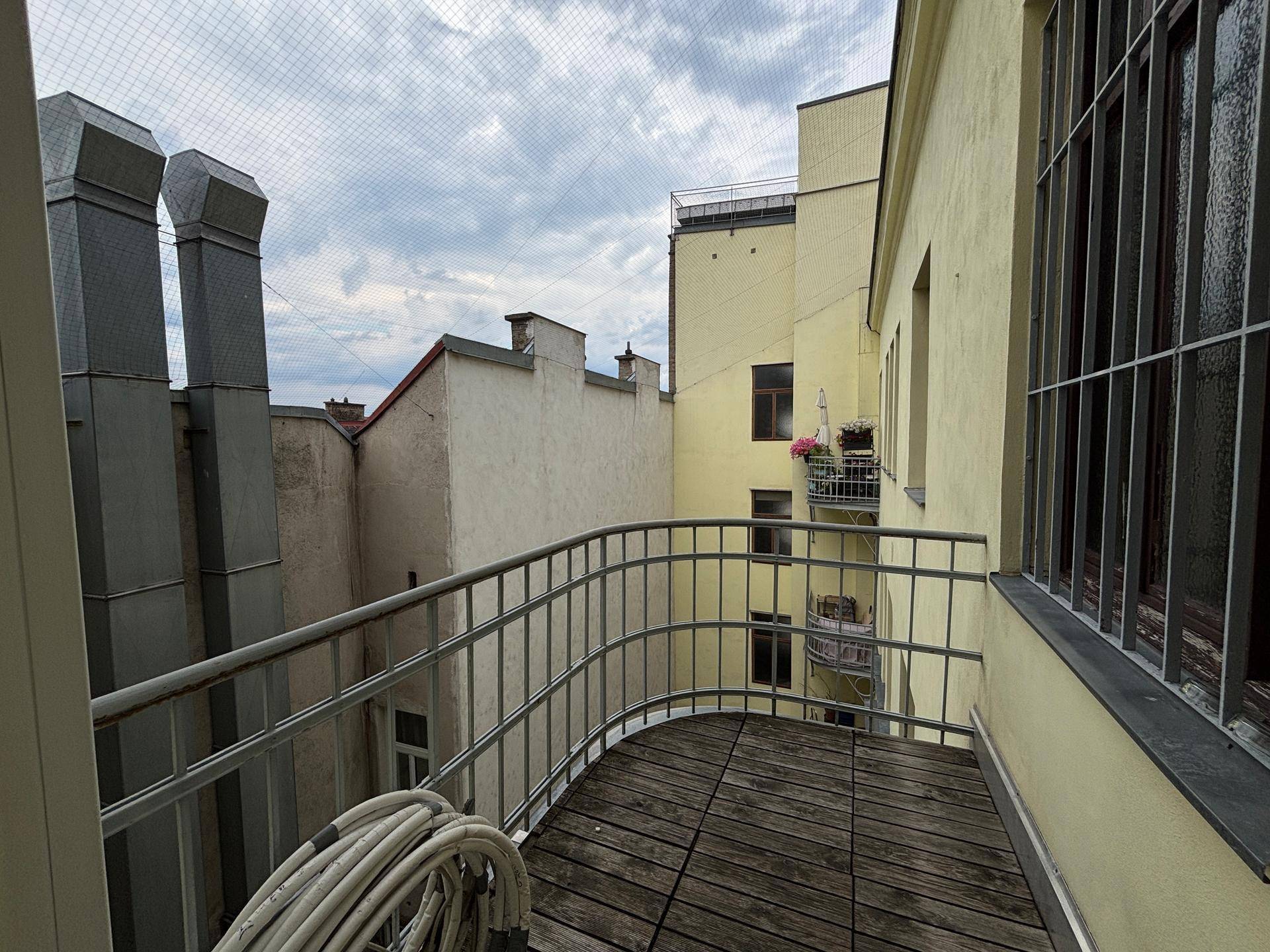 Kleiner Balkon mit Holzboden und Metallgeländer, umgeben von Stadtgebäuden, bietet einen Außenbereich.